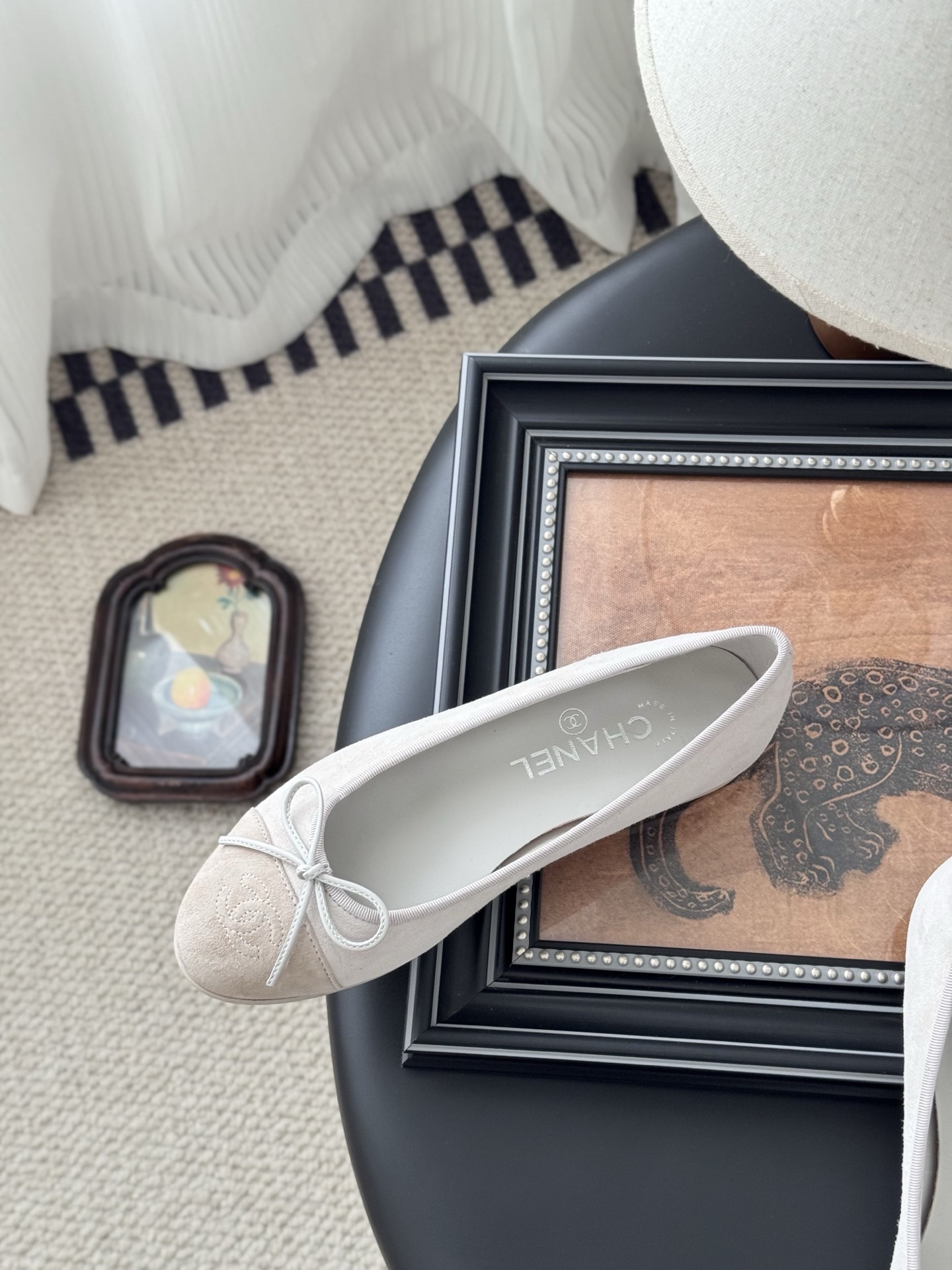 Pair of Chanel beige suede ballet flats with CC logo on the toe cap and white bow detail, placed next to a black Chanel box. - Hình 8