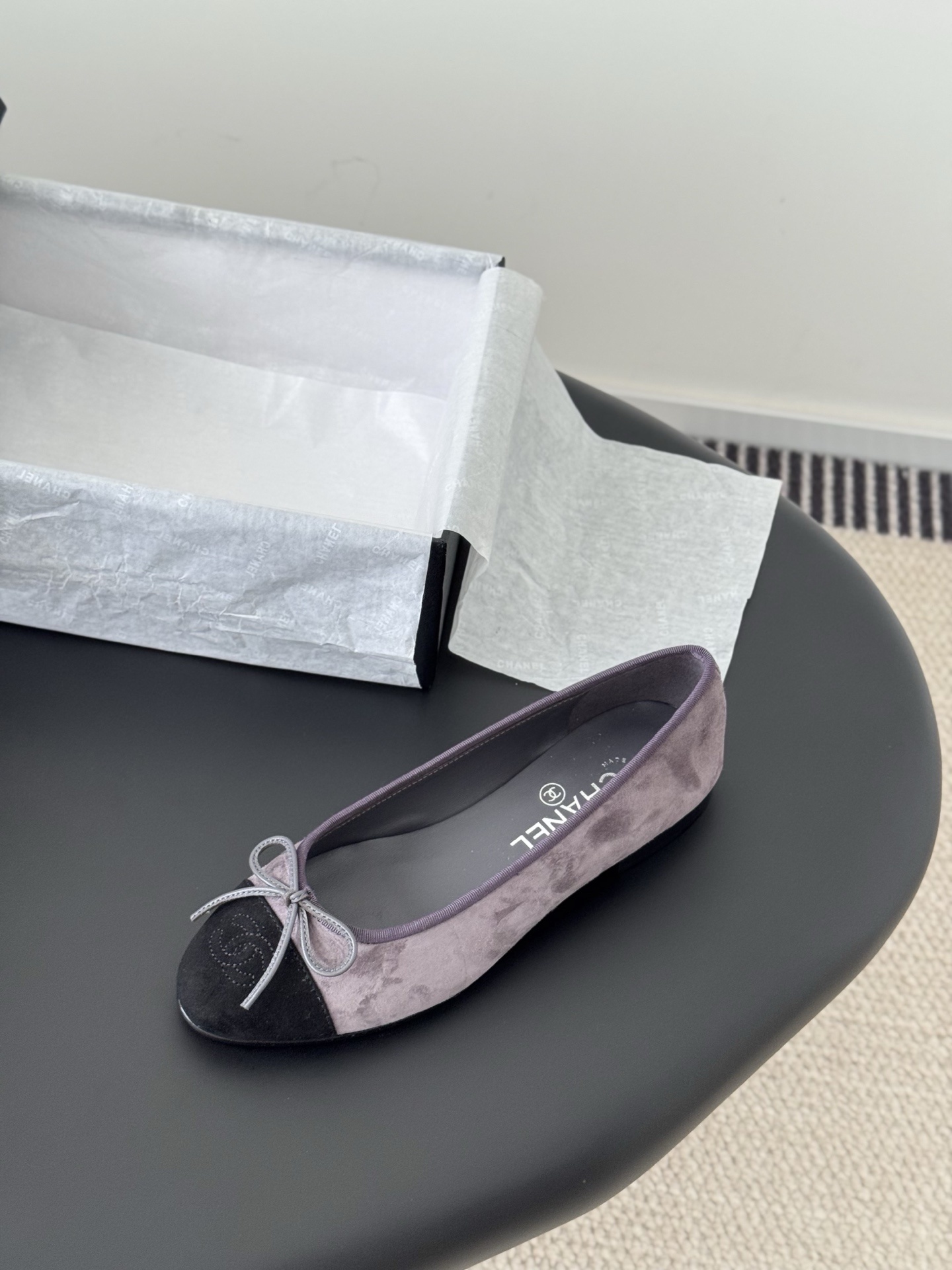 A pair of Chanel mauve suede ballet flats with black toe caps and bow detail next to an original Chanel box. - Hình 5