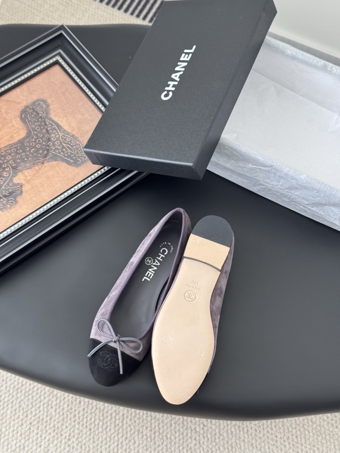 A pair of Chanel mauve suede ballet flats with black toe caps and bow detail next to an original Chanel box. - Hình 4