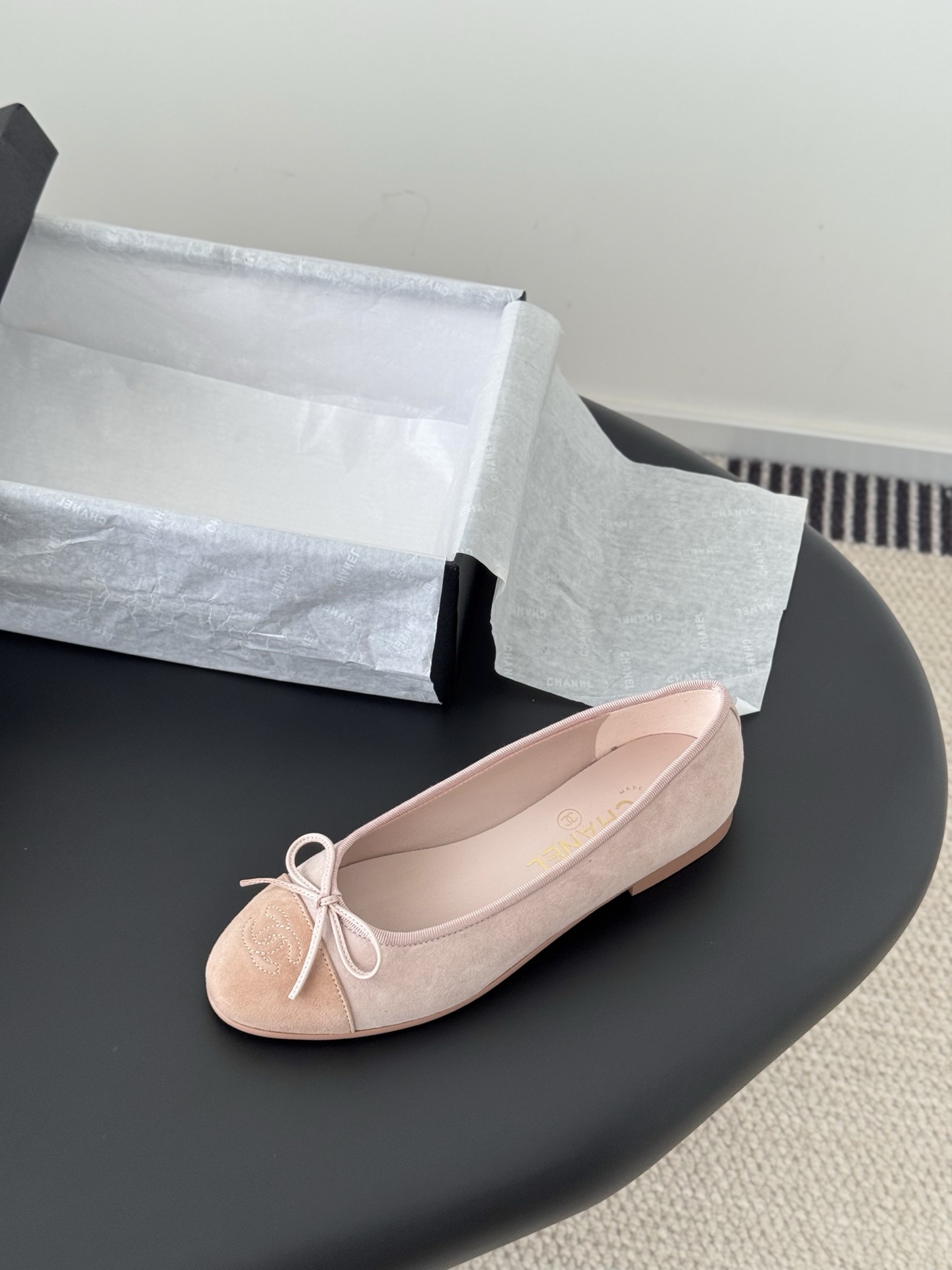 Pair of Chanel pink suede ballet flats with CC logo and bow detail next to a black shoe box - Hình 5