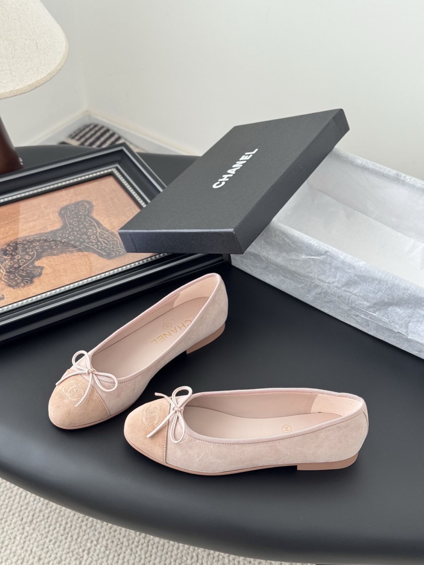 Pair of Chanel pink suede ballet flats with CC logo and bow detail next to a black shoe box - Hình 2