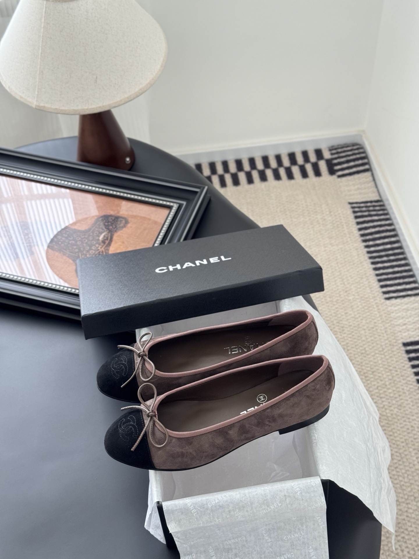 Luxury Chanel brown suede ballerina flats with black cap toe and bow detail placed next to a Chanel shoe box. - Hình 9
