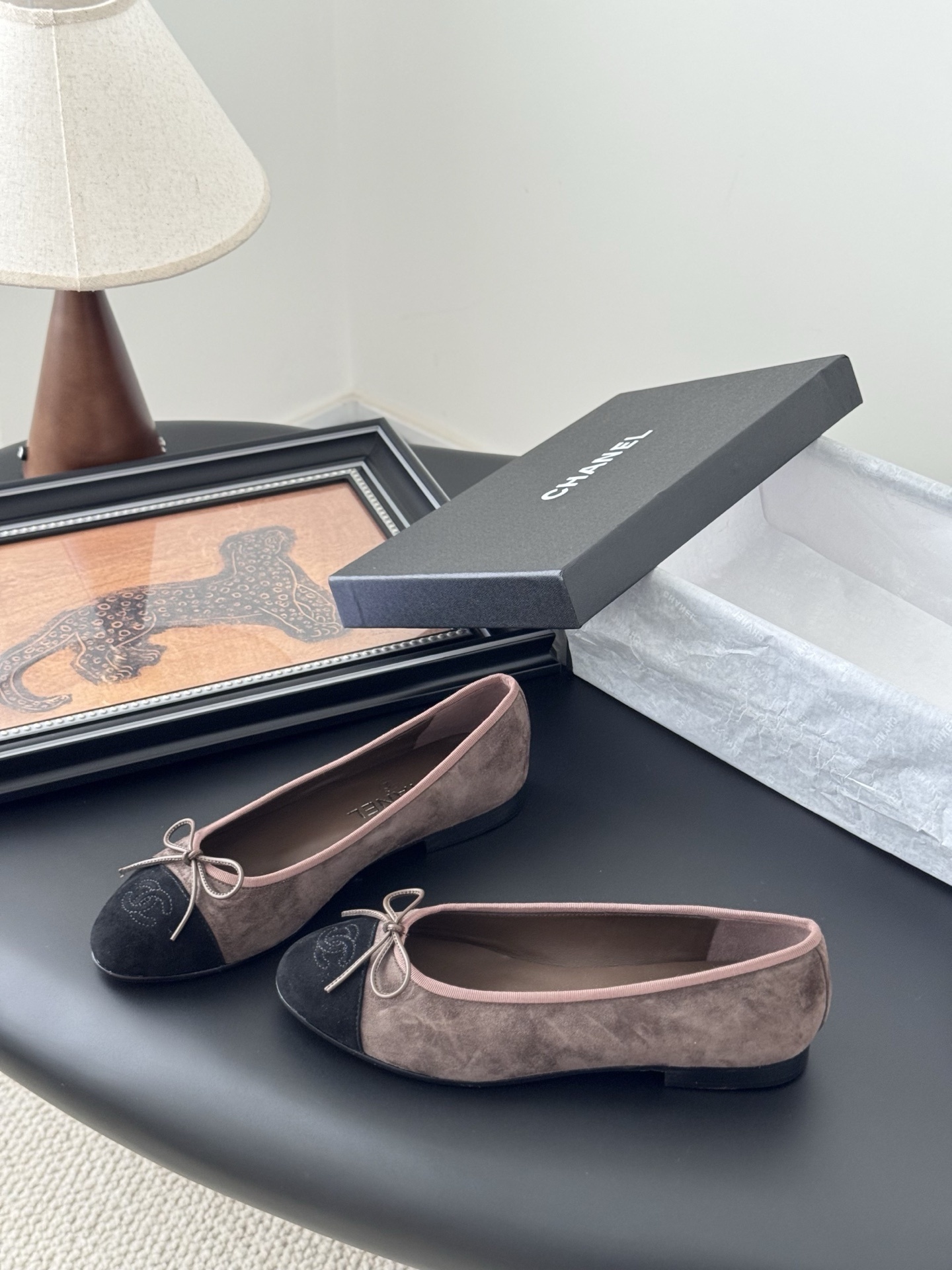 Luxury Chanel brown suede ballerina flats with black cap toe and bow detail placed next to a Chanel shoe box. - Hình 2
