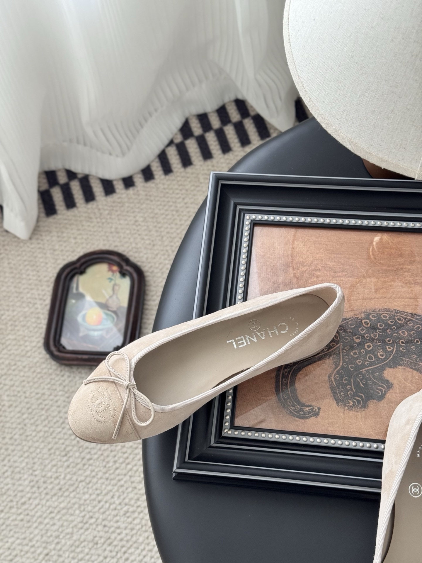 Pair of beige Chanel suede ballet flats with embossed CC logo and bow detail next to a black Chanel shoe box. - Hình 8