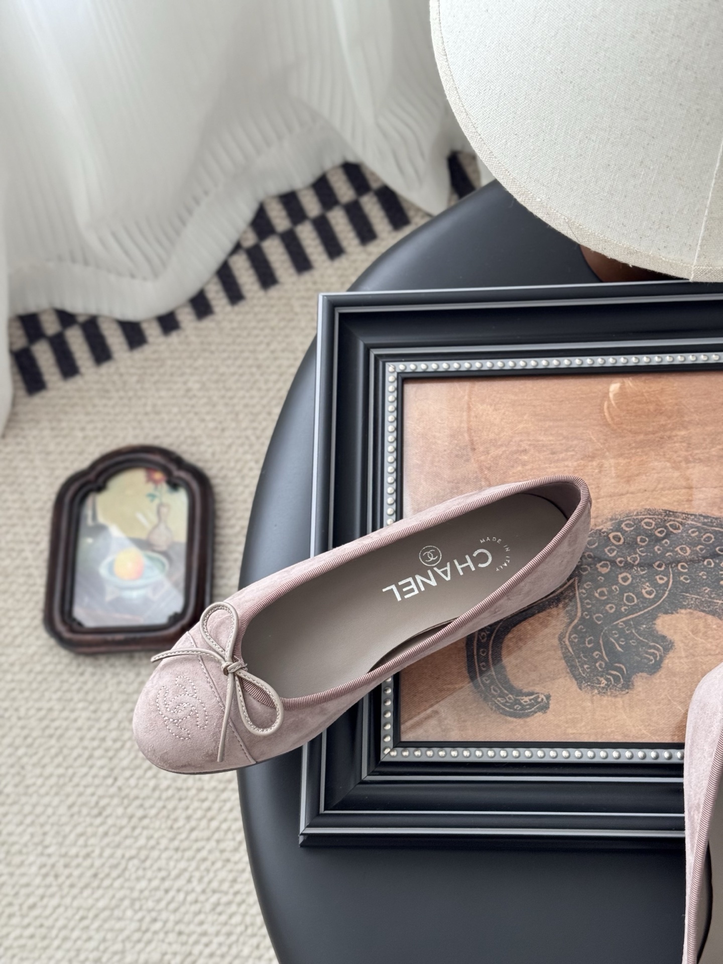 A pair of luxury pink Chanel suede ballet flats with bow and CC logo next to a black Chanel box on a black surface. - Hình 8
