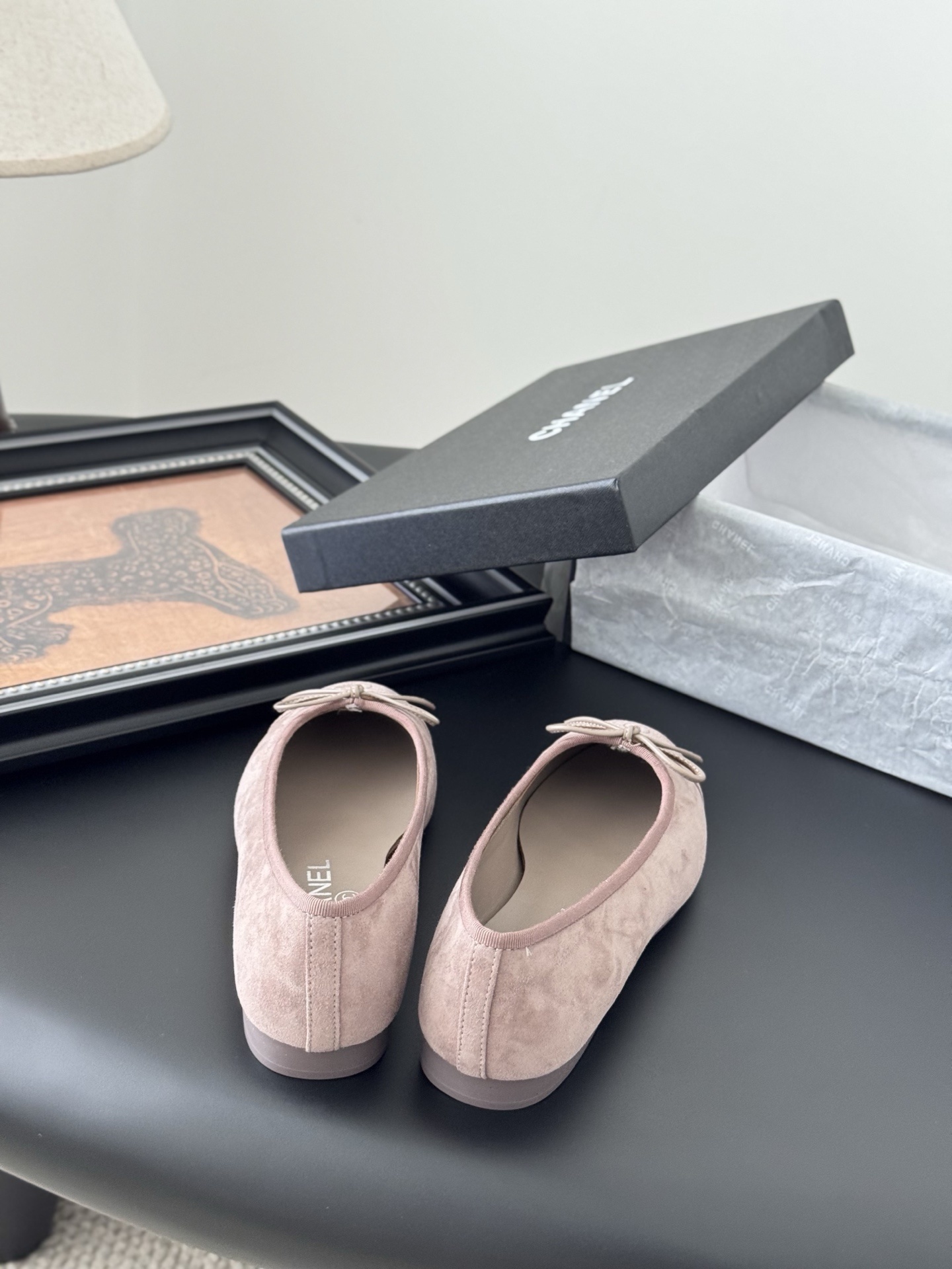 A pair of luxury pink Chanel suede ballet flats with bow and CC logo next to a black Chanel box on a black surface. - Hình 6