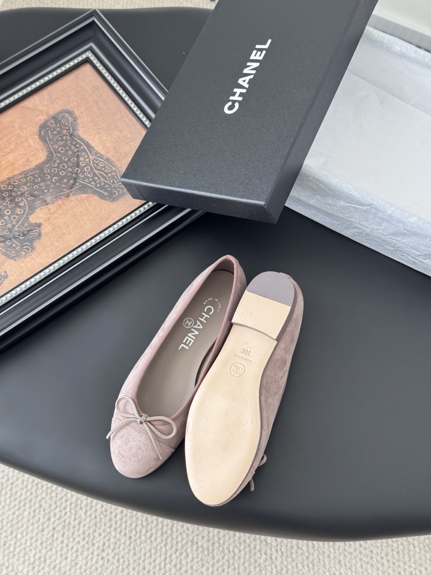 A pair of luxury pink Chanel suede ballet flats with bow and CC logo next to a black Chanel box on a black surface. - Hình 4