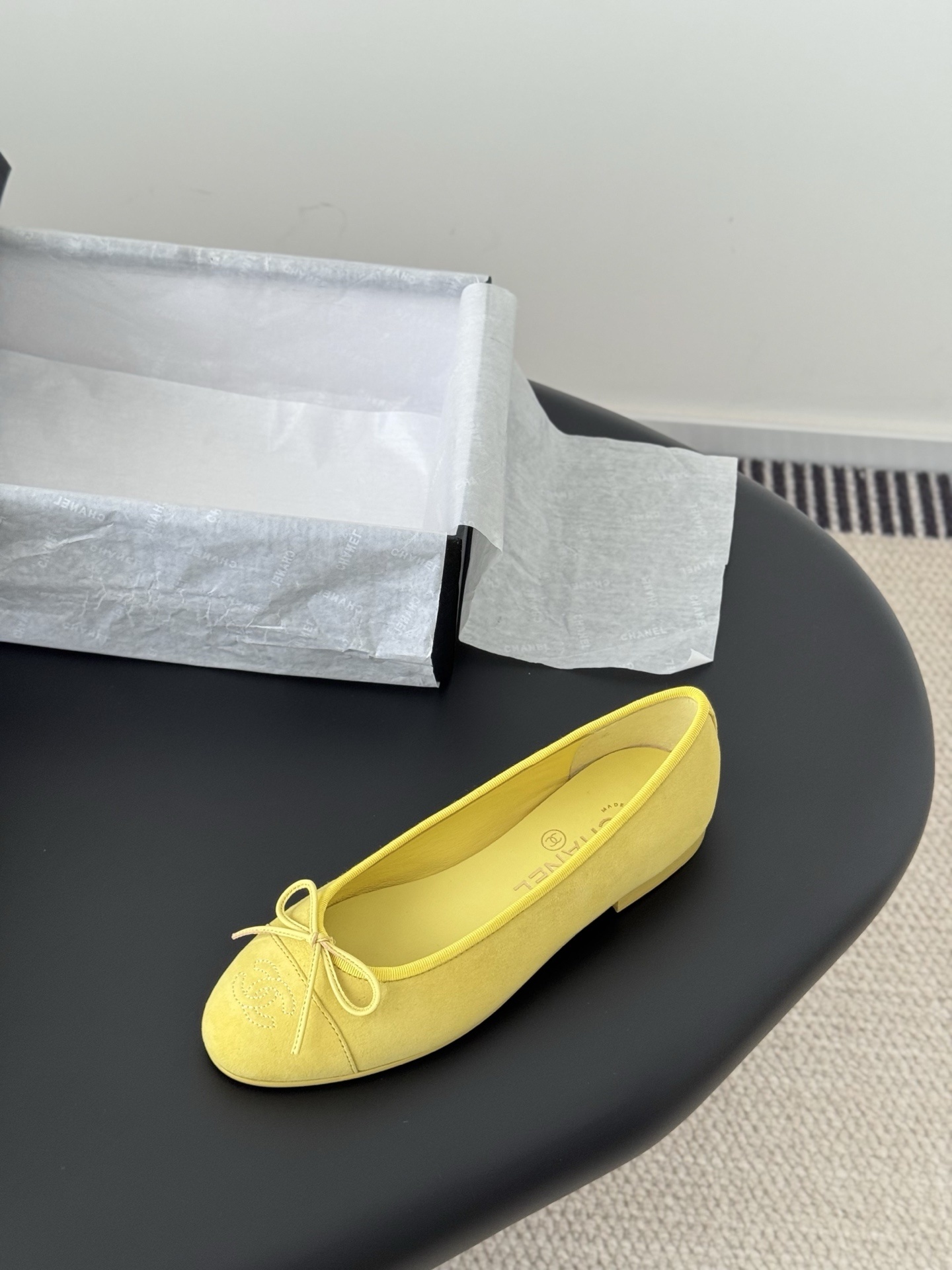 A pair of yellow Chanel suede ballerina flats with a bow and embroidered logo next to their original black box. - Hình 5
