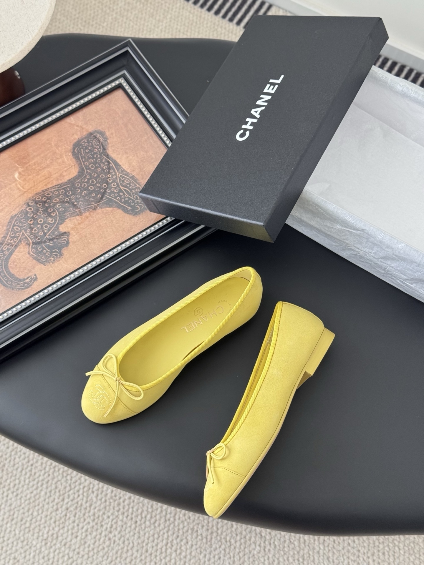 A pair of yellow Chanel suede ballerina flats with a bow and embroidered logo next to their original black box. - Hình 3