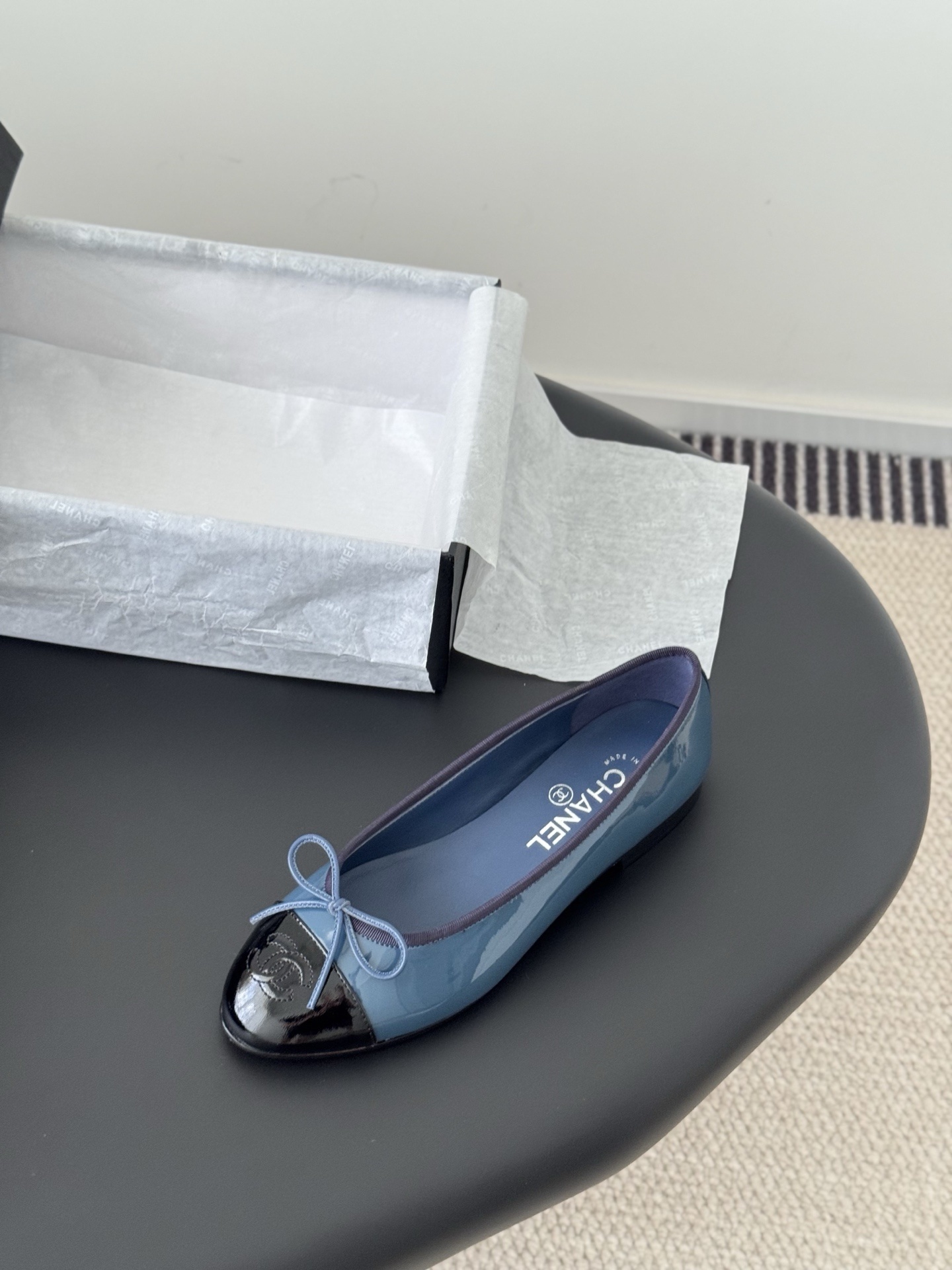 A pair of Chanel two-tone patent leather ballet flats in blue and black with a bow detail and CC logo, displayed with the original Chanel box. - Hình 5