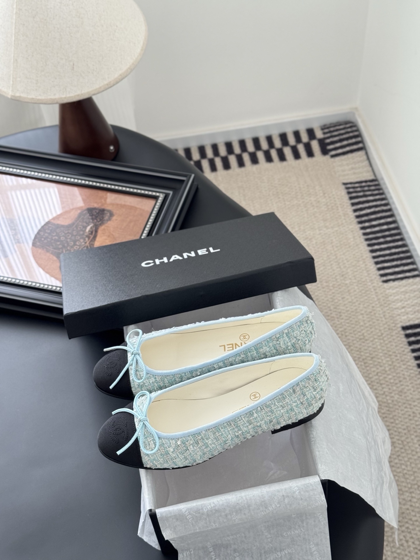 A pair of Chanel light blue tweed ballerina flats with black cap toe and bow detail next to a Chanel luxury box. - Hình 9