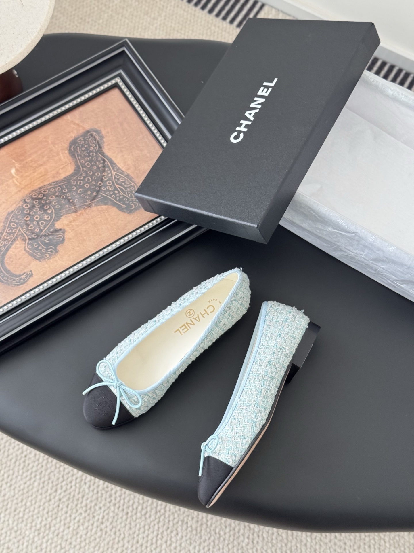 A pair of Chanel light blue tweed ballerina flats with black cap toe and bow detail next to a Chanel luxury box. - Hình 3