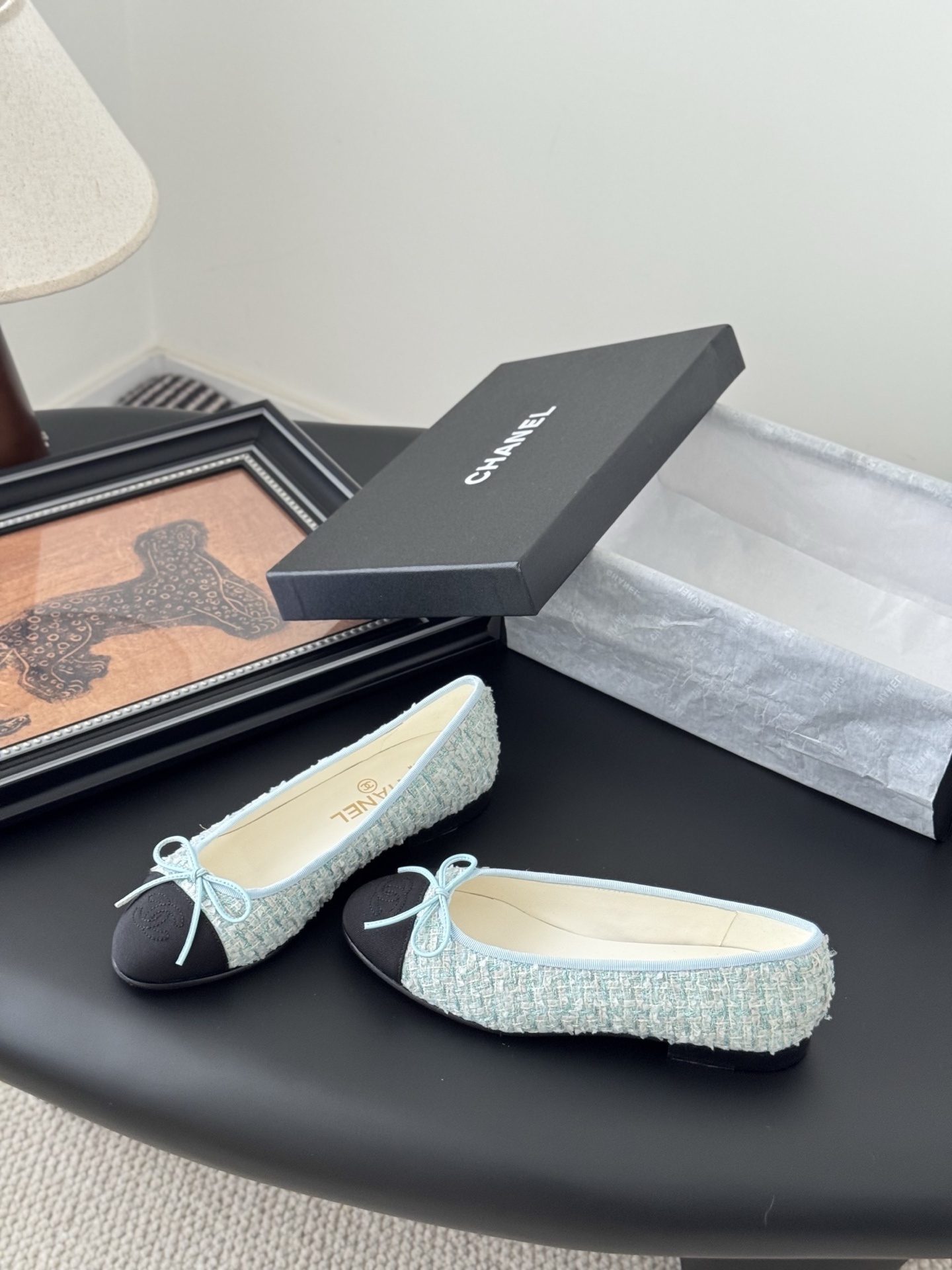 A pair of Chanel light blue tweed ballerina flats with black cap toe and bow detail next to a Chanel luxury box. - Hình 2