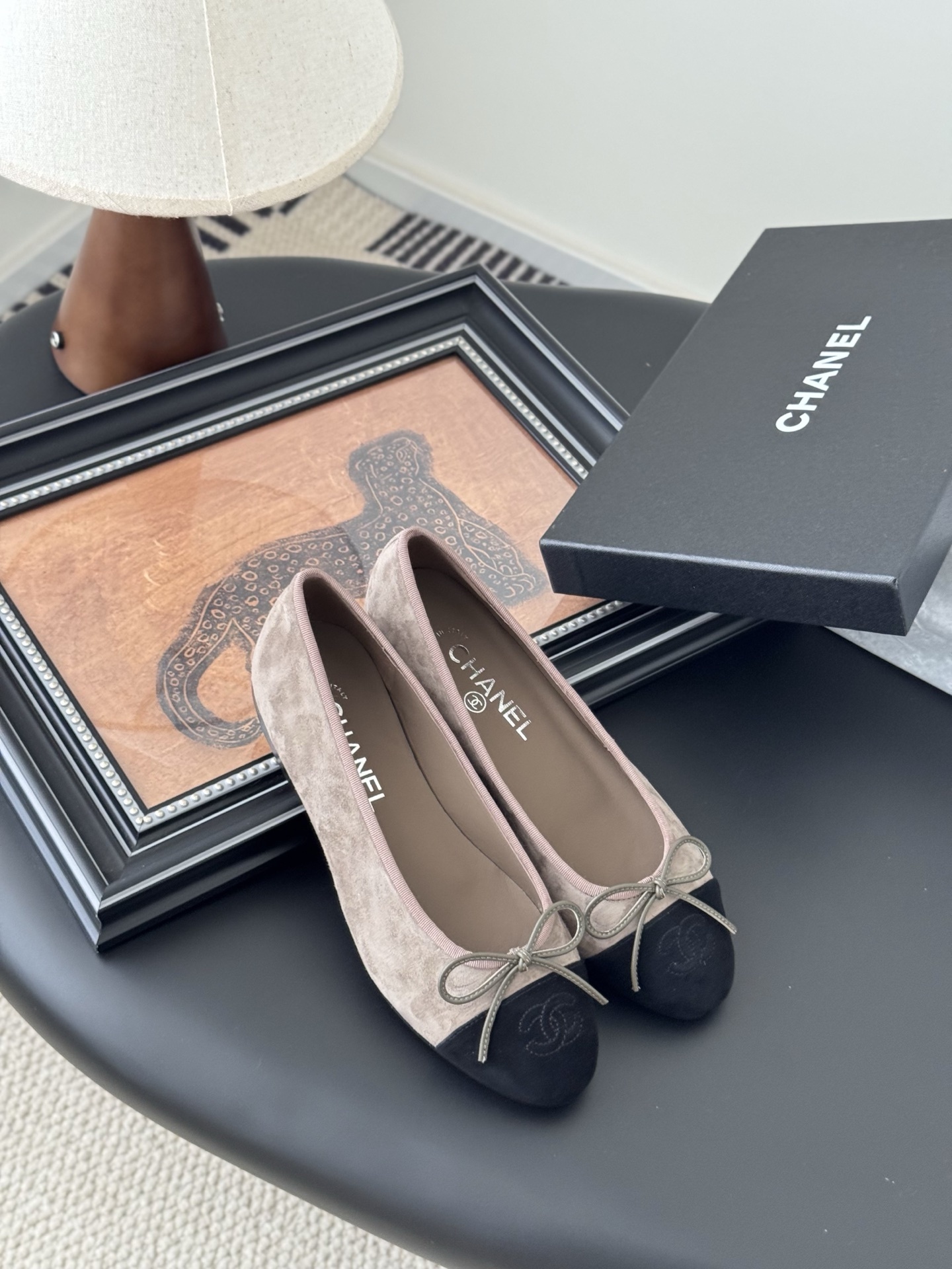 Luxury Chanel beige suede ballerina flats with black CC logo toe cap placed next to a black Chanel shoe box on a dark table. - Hình 7