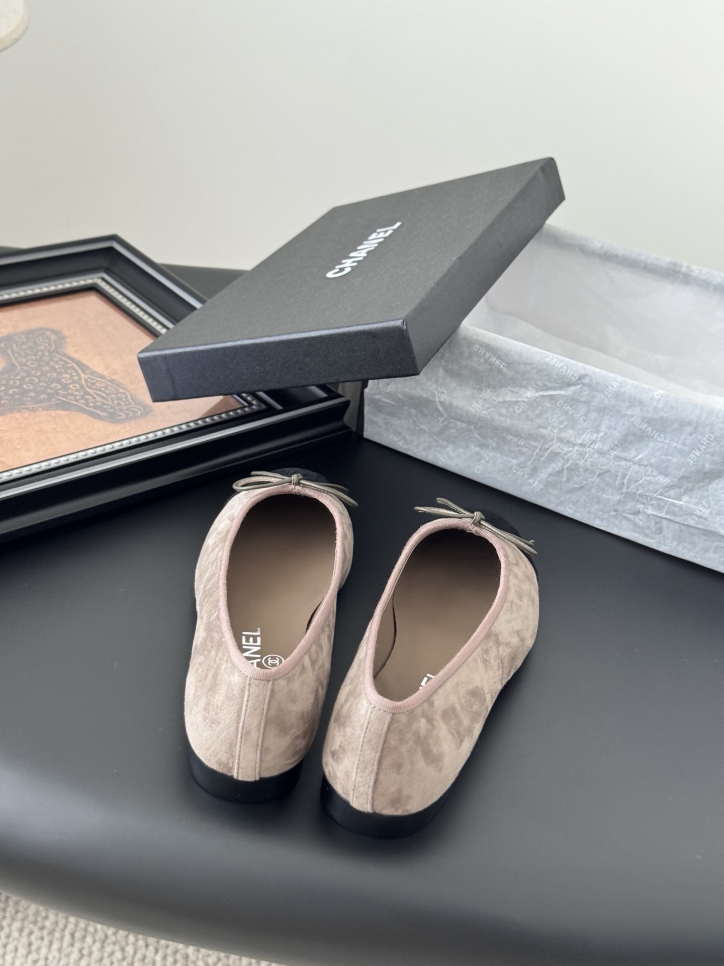 Luxury Chanel beige suede ballerina flats with black CC logo toe cap placed next to a black Chanel shoe box on a dark table. - Hình 6