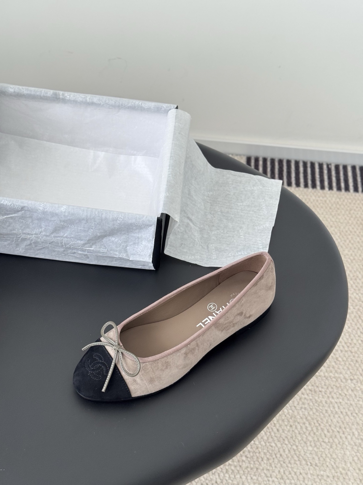 Luxury Chanel beige suede ballerina flats with black CC logo toe cap placed next to a black Chanel shoe box on a dark table. - Hình 5