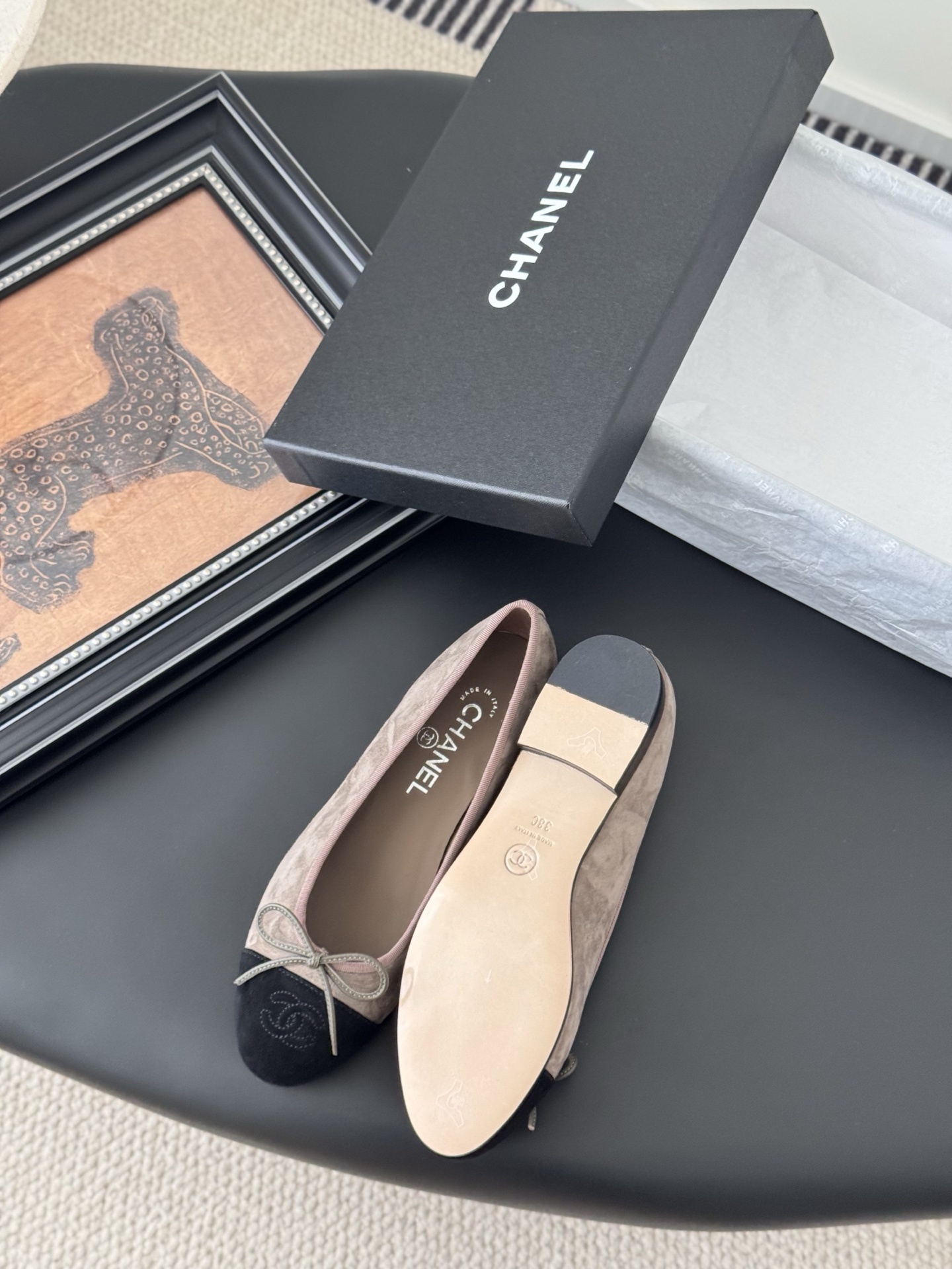 Luxury Chanel beige suede ballerina flats with black CC logo toe cap placed next to a black Chanel shoe box on a dark table. - Hình 4