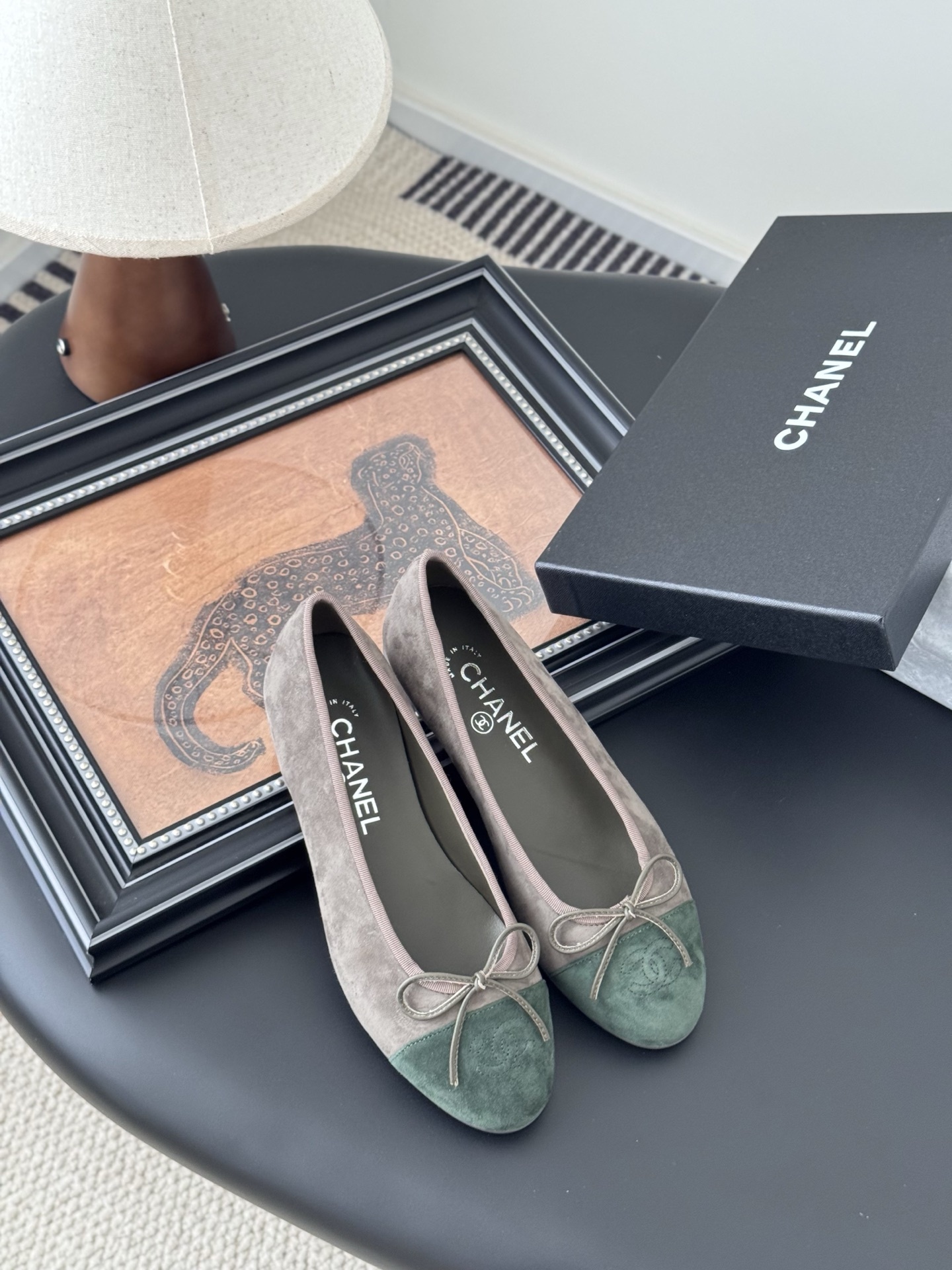 A pair of Chanel taupe suede ballerina flats with green suede cap toes and bow detail, presented next to a black Chanel shoe box. - Hình 7