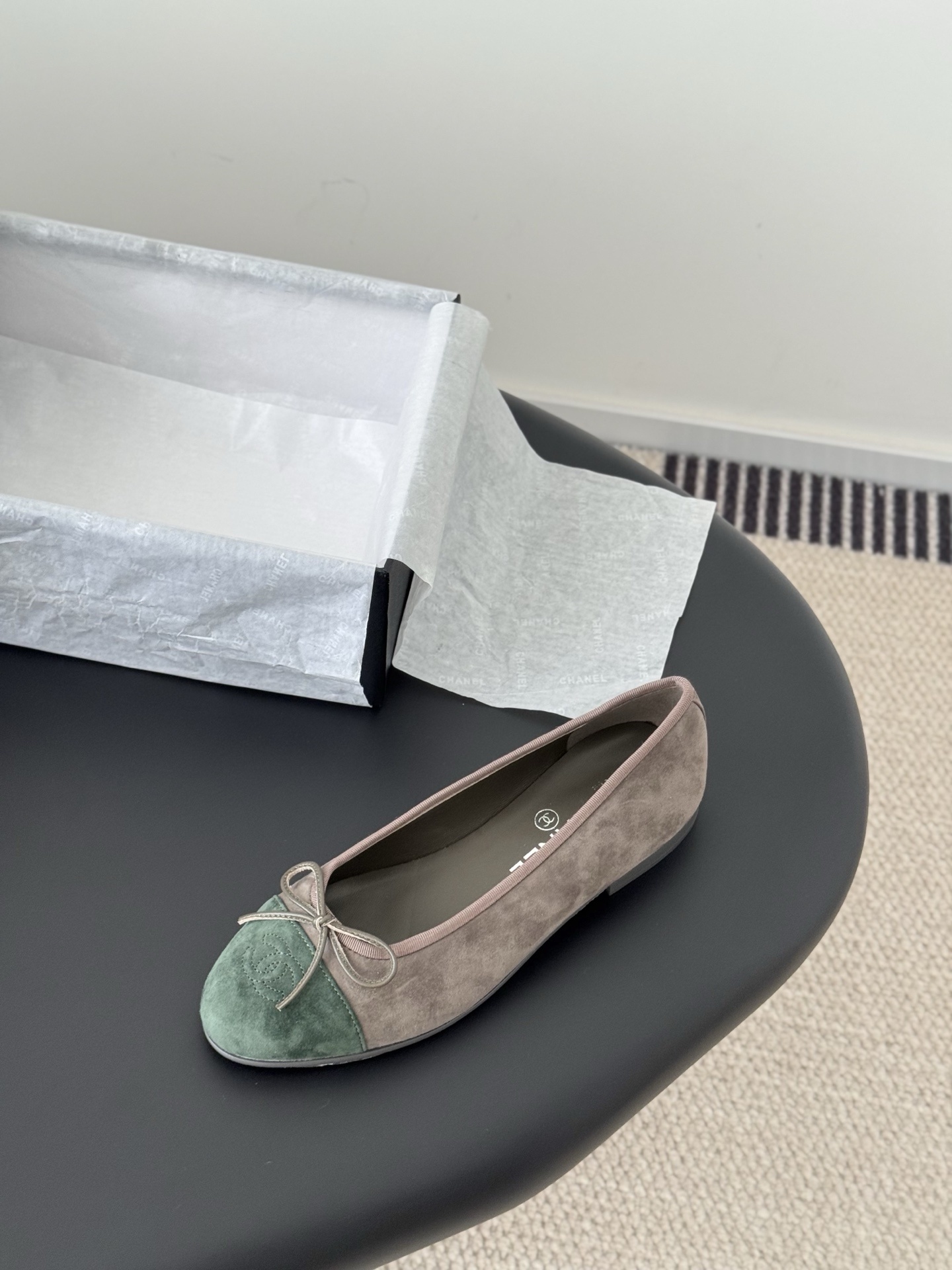 A pair of Chanel taupe suede ballerina flats with green suede cap toes and bow detail, presented next to a black Chanel shoe box. - Hình 5