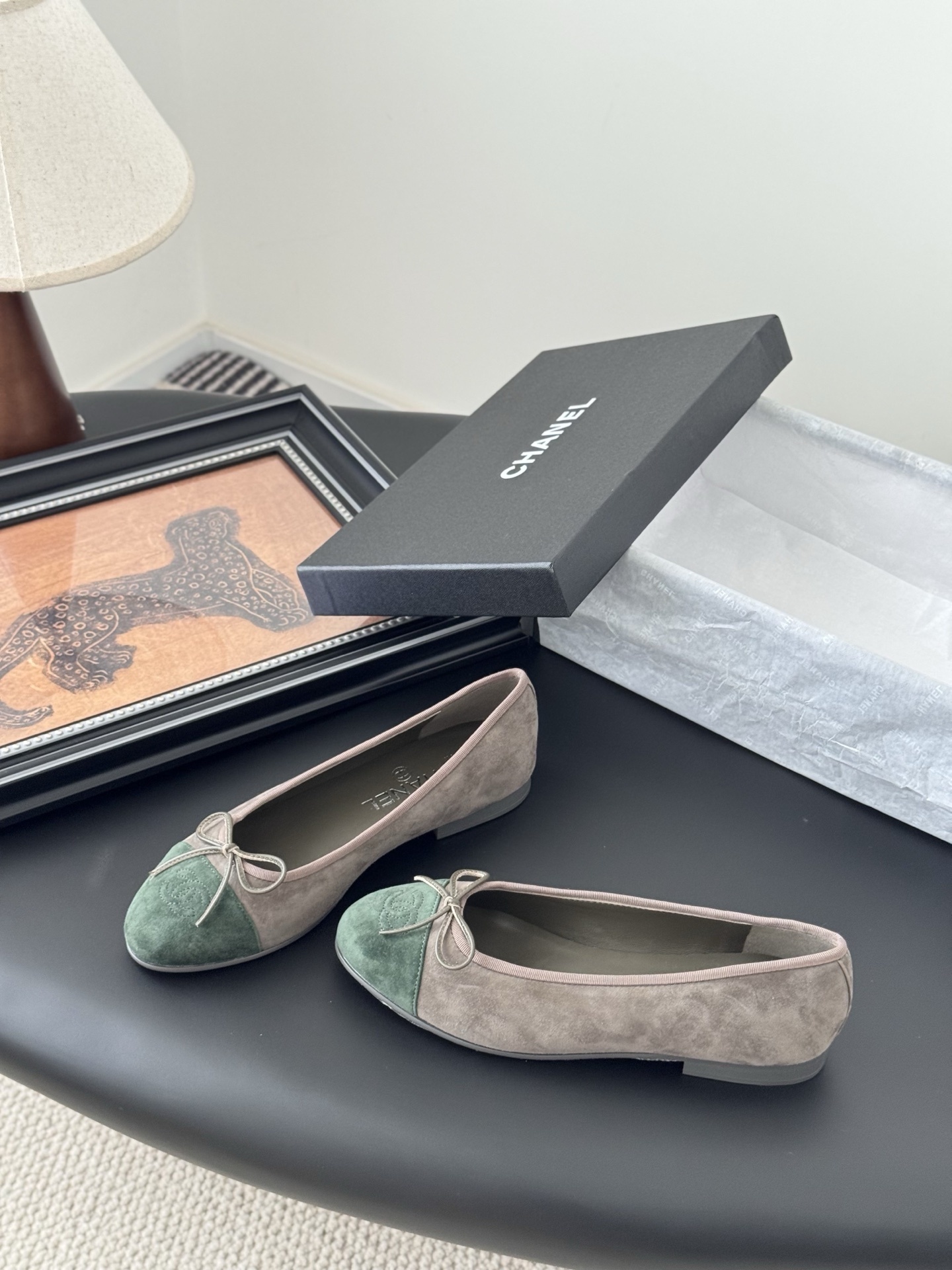 A pair of Chanel taupe suede ballerina flats with green suede cap toes and bow detail, presented next to a black Chanel shoe box. - Hình 2