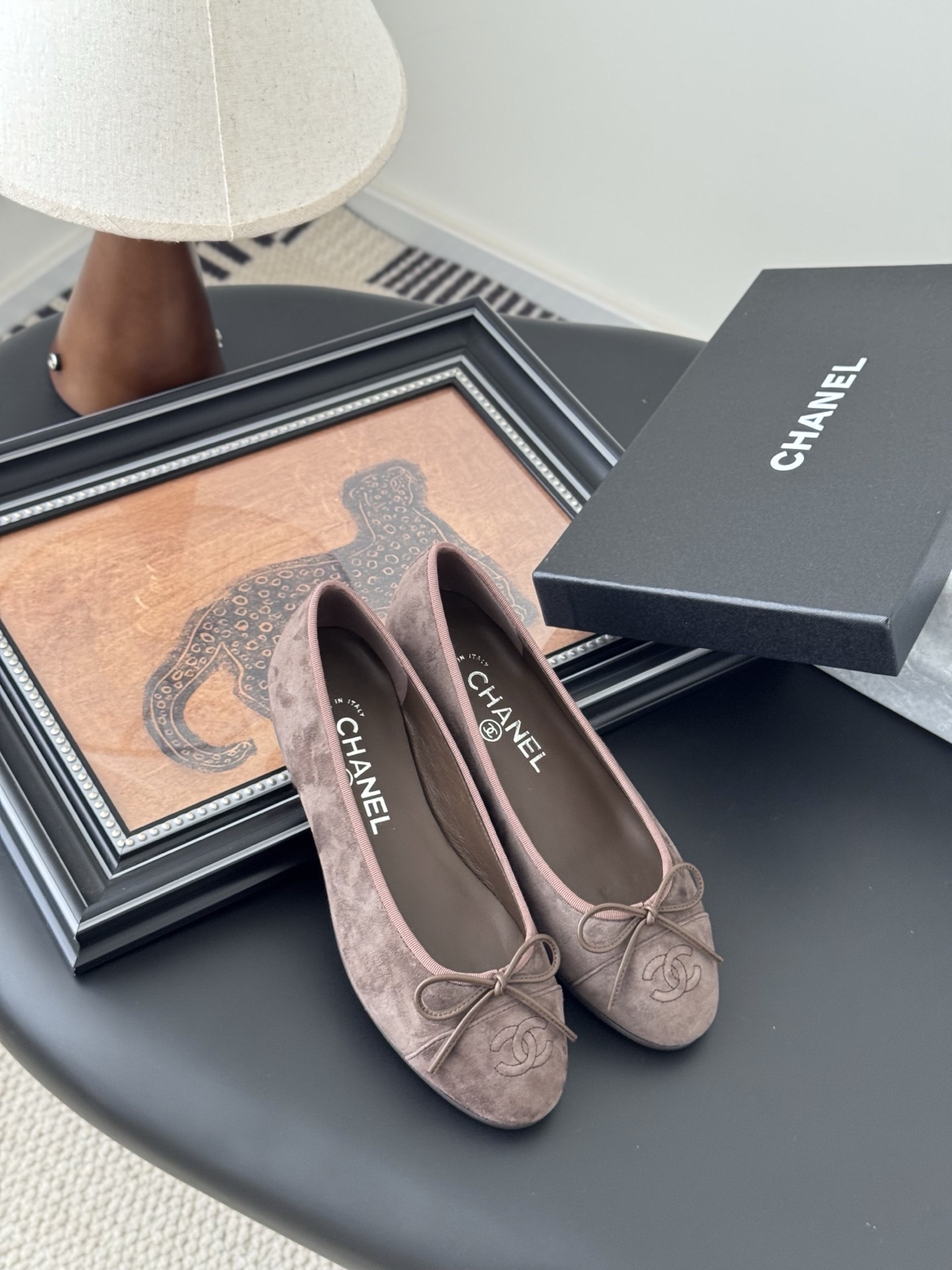 A pair of taupe Chanel suede ballet flats with embroidered CC logo and bow detail next to an original Chanel box - Hình 7