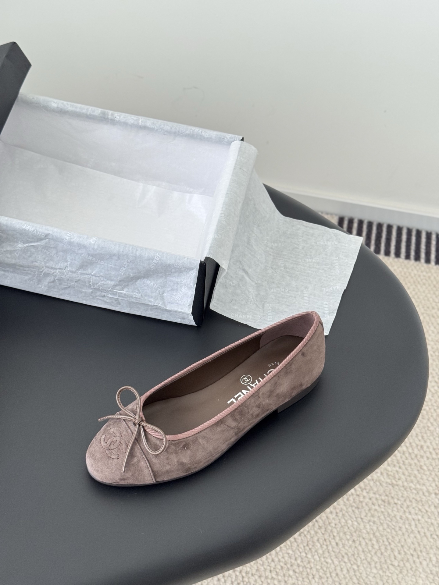 A pair of taupe Chanel suede ballet flats with embroidered CC logo and bow detail next to an original Chanel box - Hình 5