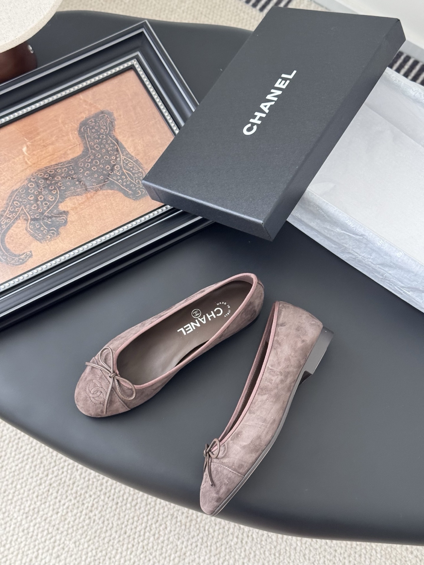 A pair of taupe Chanel suede ballet flats with embroidered CC logo and bow detail next to an original Chanel box - Hình 3