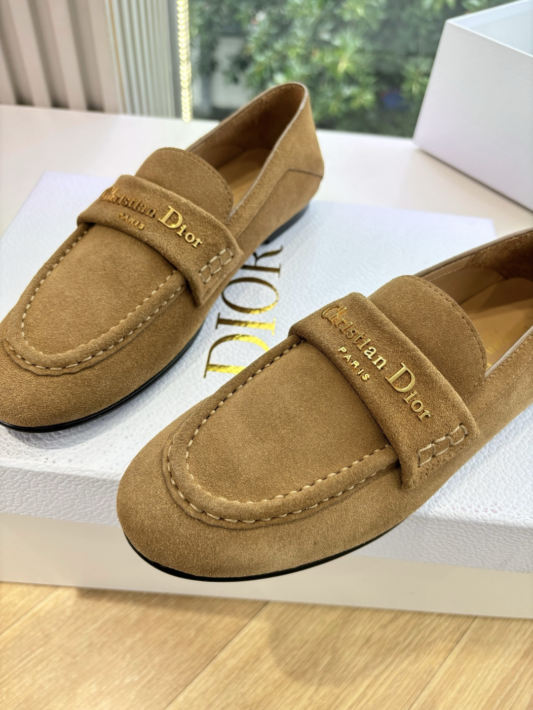 A pair of Christian Dior tan suede loafers with gold logo lettering displayed in a white Dior box. - Hình 8