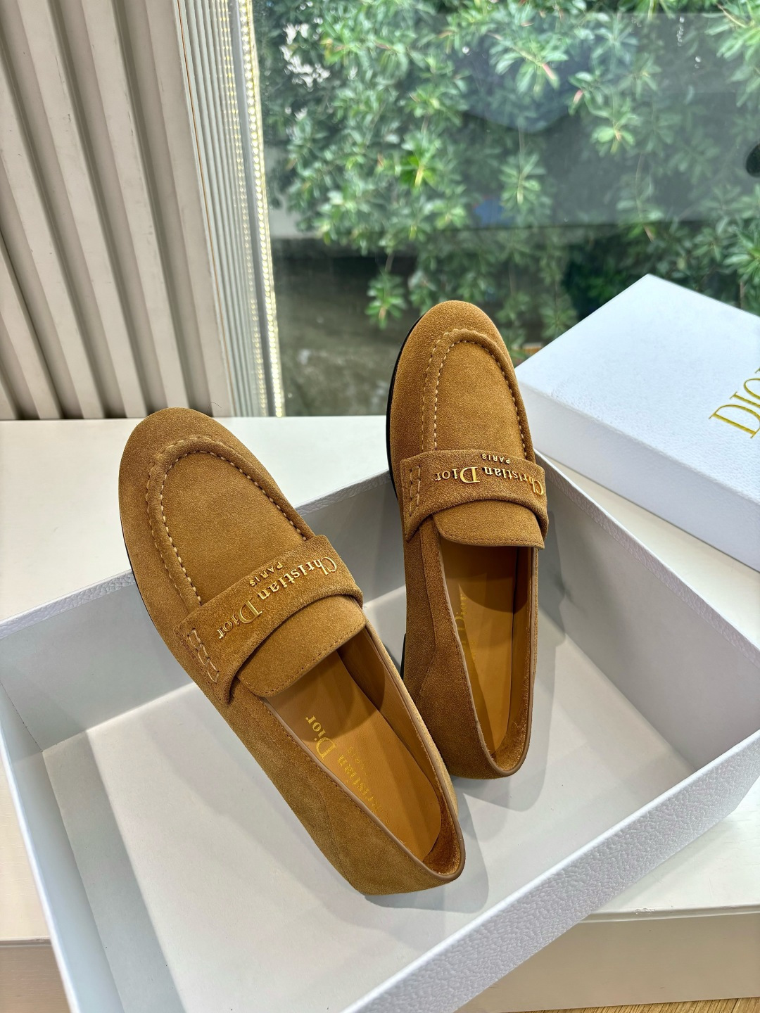 A pair of Christian Dior tan suede loafers with gold logo lettering displayed in a white Dior box. - Hình 2