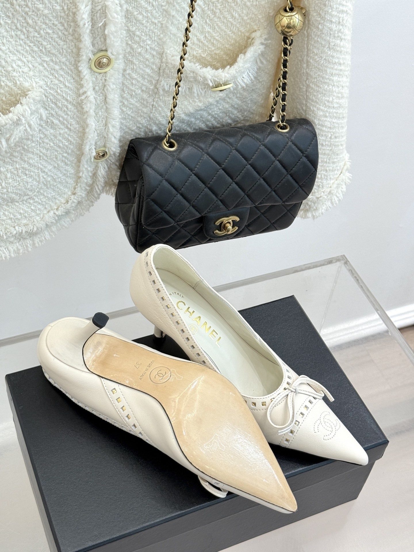 Luxury Chanel white leather pointed-toe kitten heels with bow and embossed CC logo on a black shoe box. - Hình 9