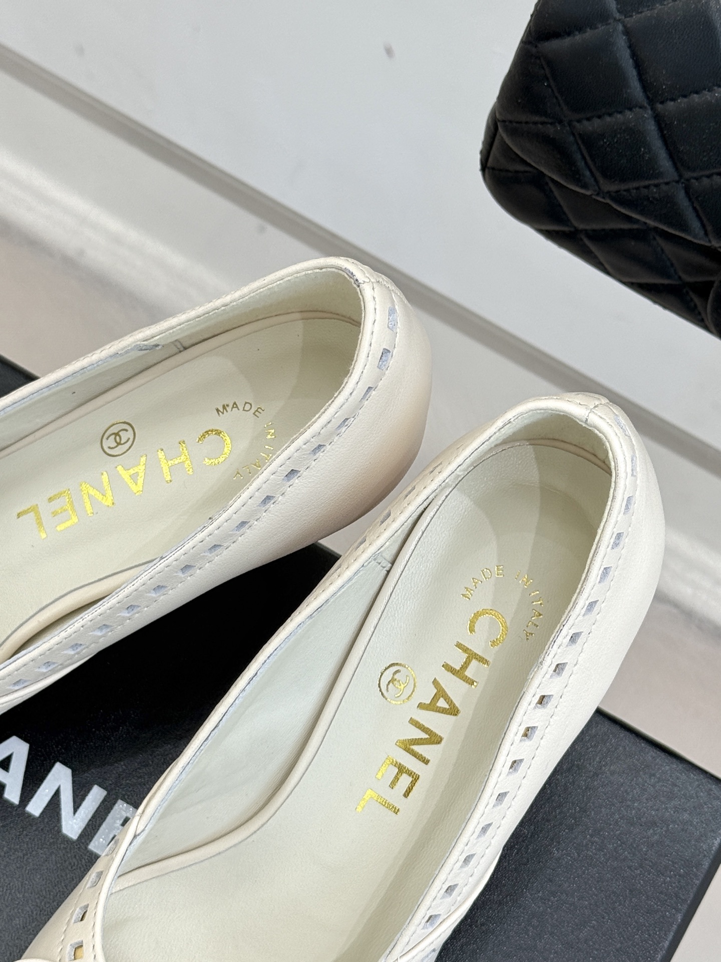 Luxury Chanel white leather pointed-toe kitten heels with bow and embossed CC logo on a black shoe box. - Hình 8