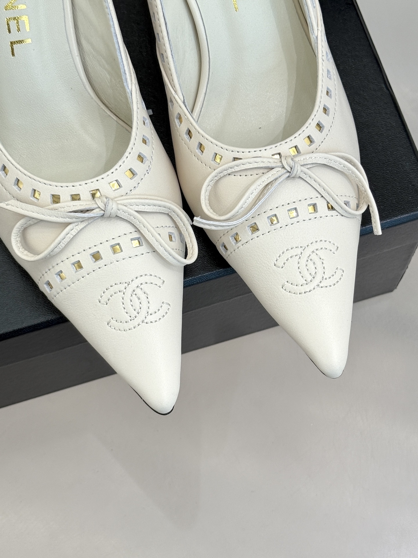 Luxury Chanel white leather pointed-toe kitten heels with bow and embossed CC logo on a black shoe box. - Hình 7