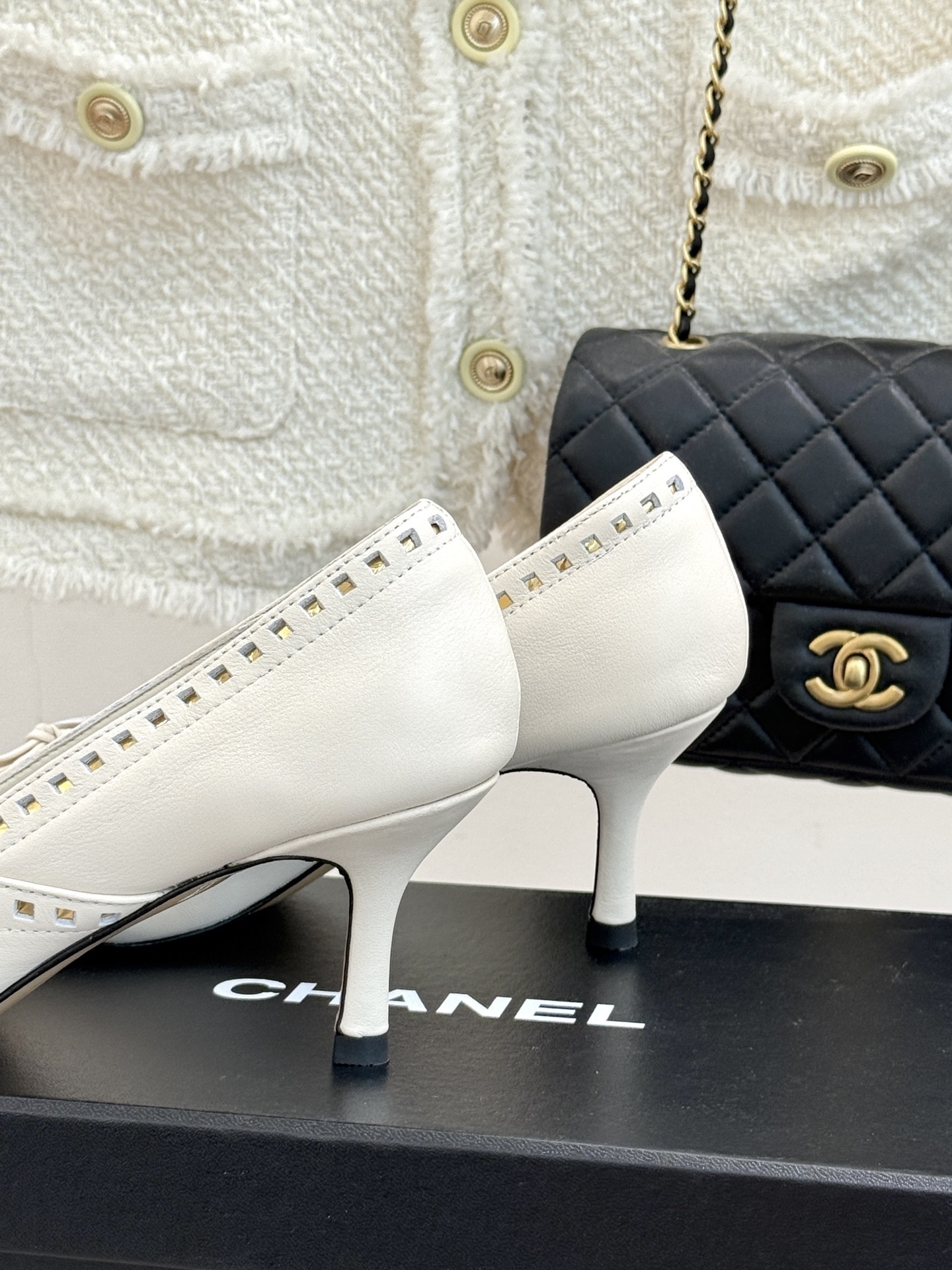 Luxury Chanel white leather pointed-toe kitten heels with bow and embossed CC logo on a black shoe box. - Hình 6