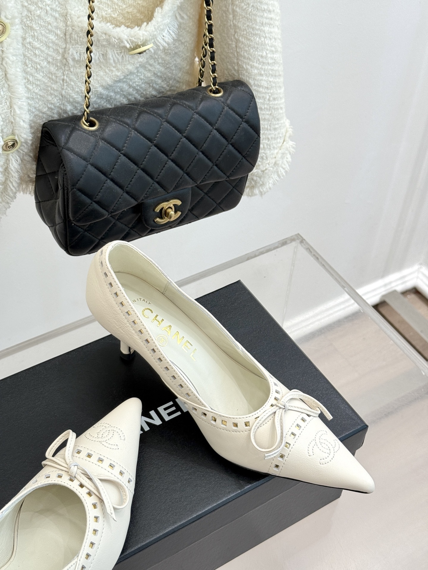 Luxury Chanel white leather pointed-toe kitten heels with bow and embossed CC logo on a black shoe box. - Hình 5
