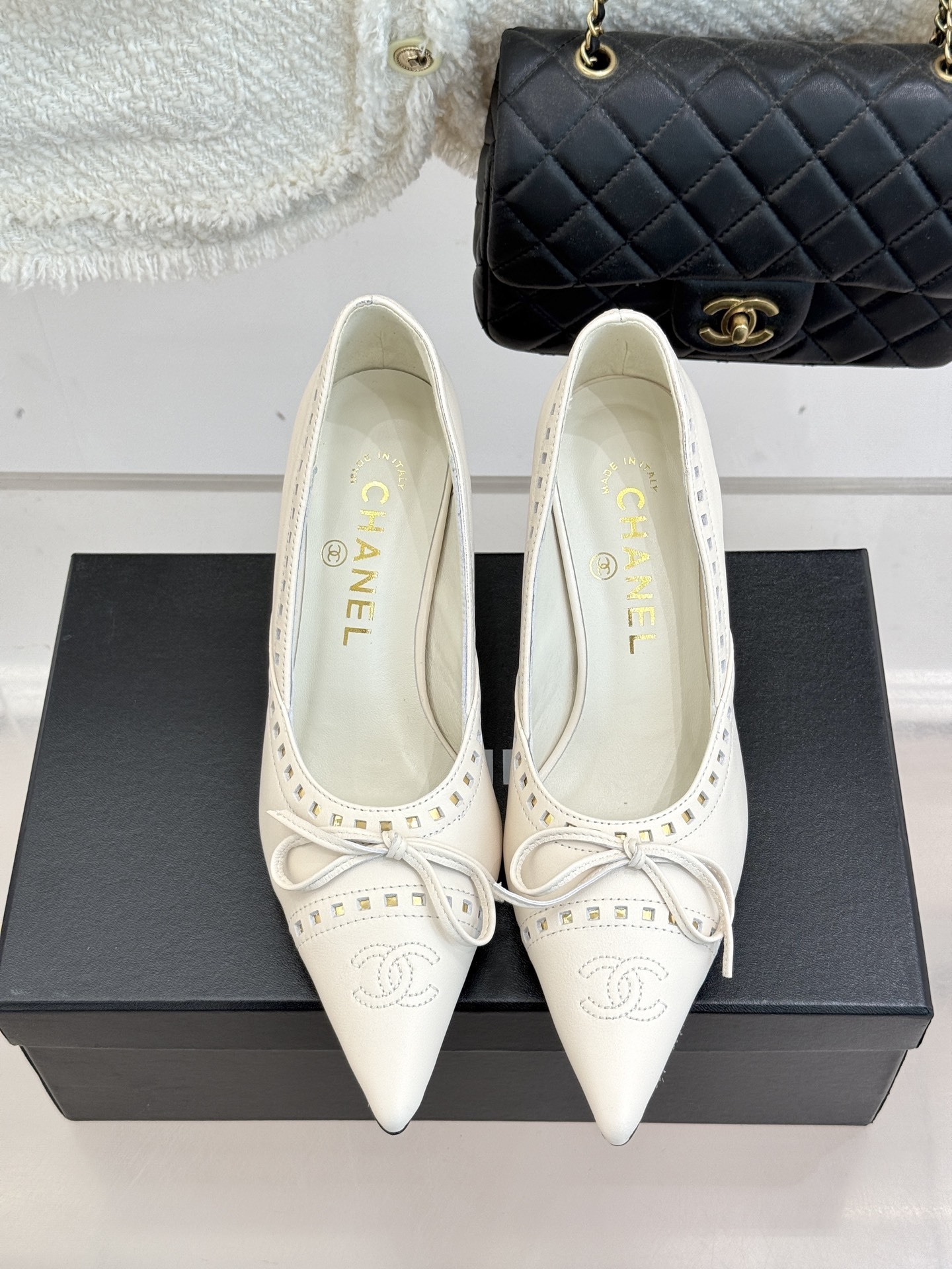 Luxury Chanel white leather pointed-toe kitten heels with bow and embossed CC logo on a black shoe box. - Hình 4