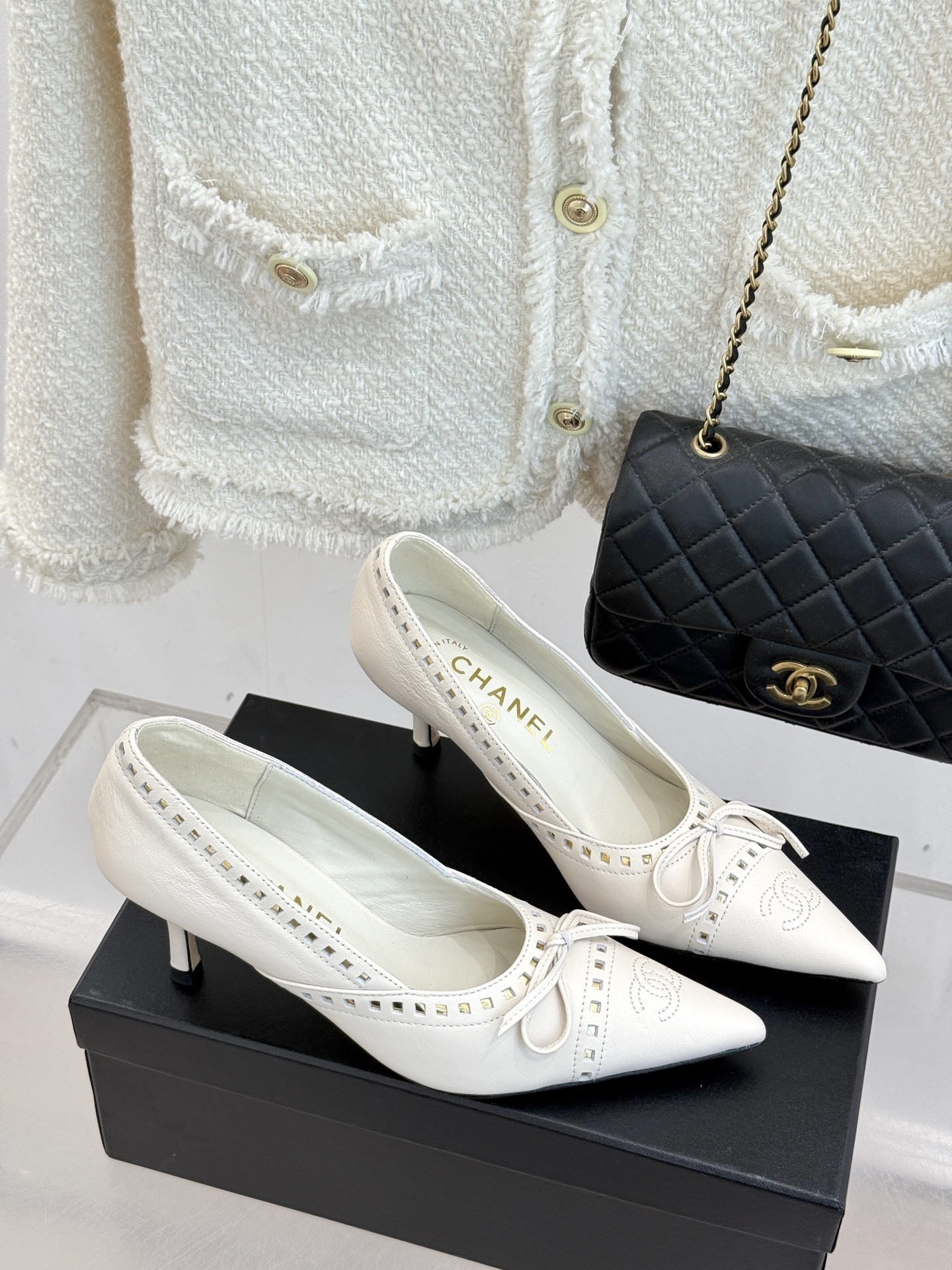 Luxury Chanel white leather pointed-toe kitten heels with bow and embossed CC logo on a black shoe box. - Hình 3