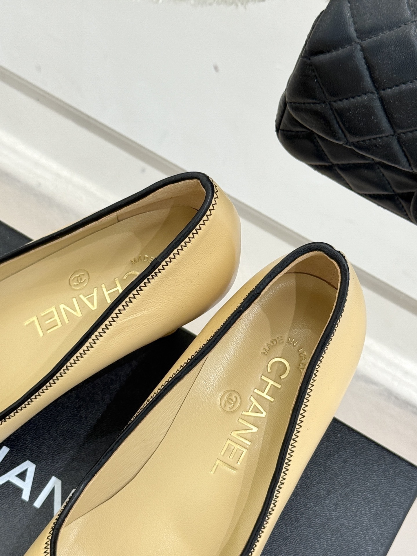 A pair of beige Chanel kitten heel pumps with black trim and CC logo on a black shoebox - Hình 8