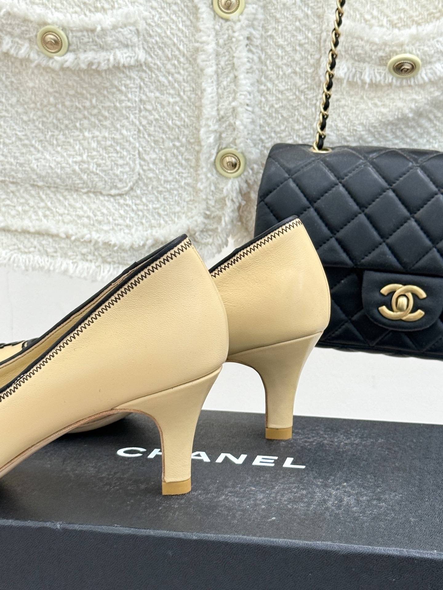 A pair of beige Chanel kitten heel pumps with black trim and CC logo on a black shoebox - Hình 6
