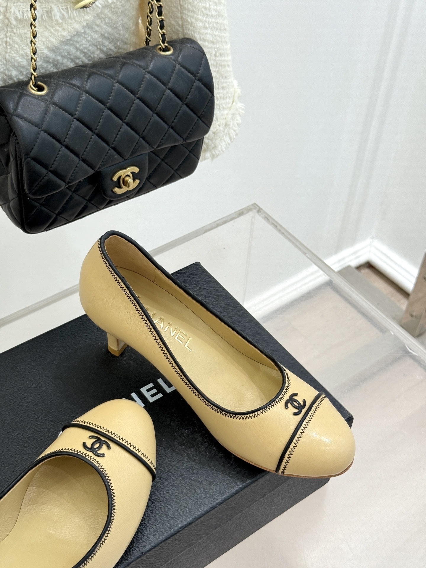 A pair of beige Chanel kitten heel pumps with black trim and CC logo on a black shoebox - Hình 5