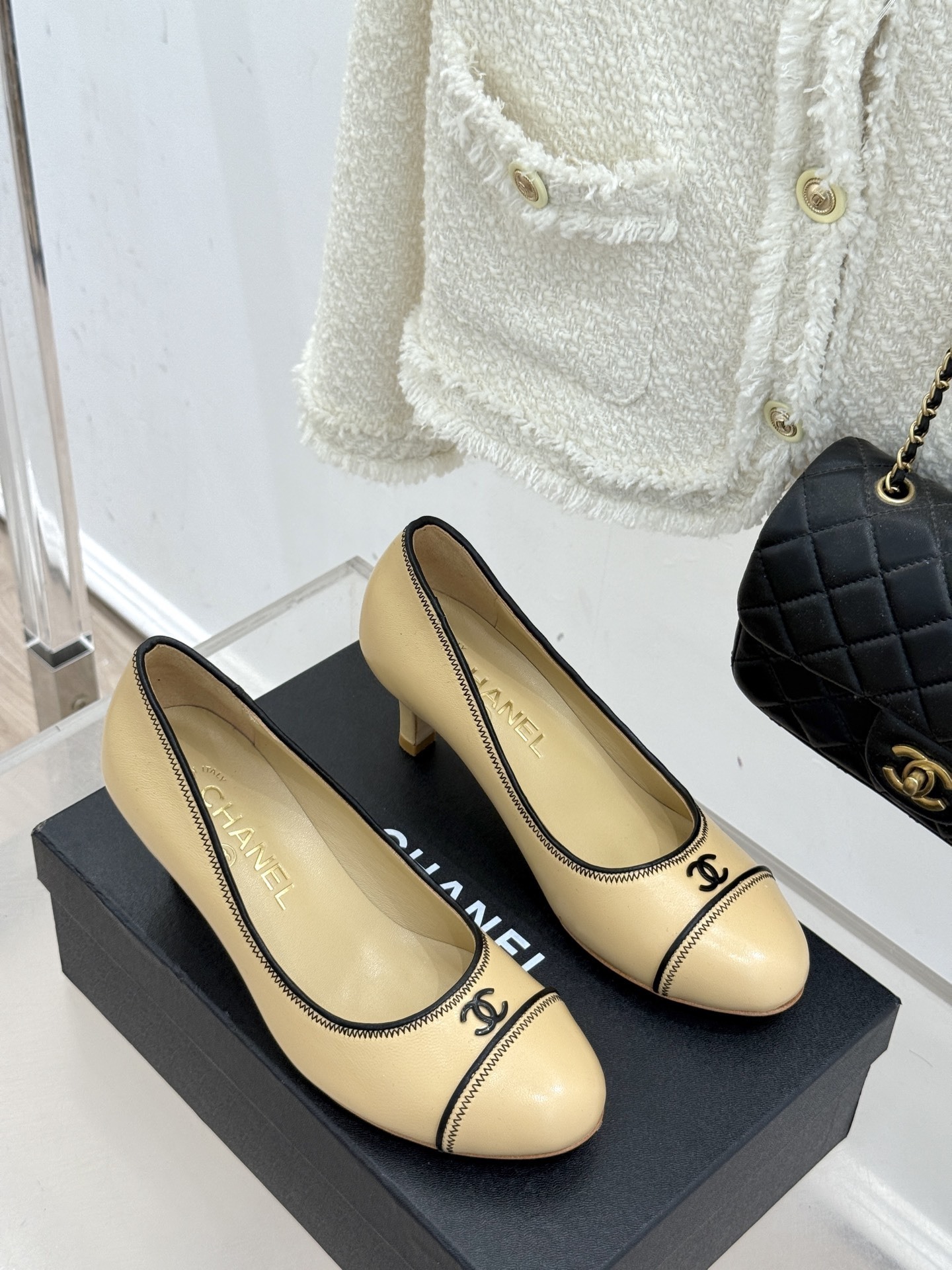 A pair of beige Chanel kitten heel pumps with black trim and CC logo on a black shoebox - Hình 3