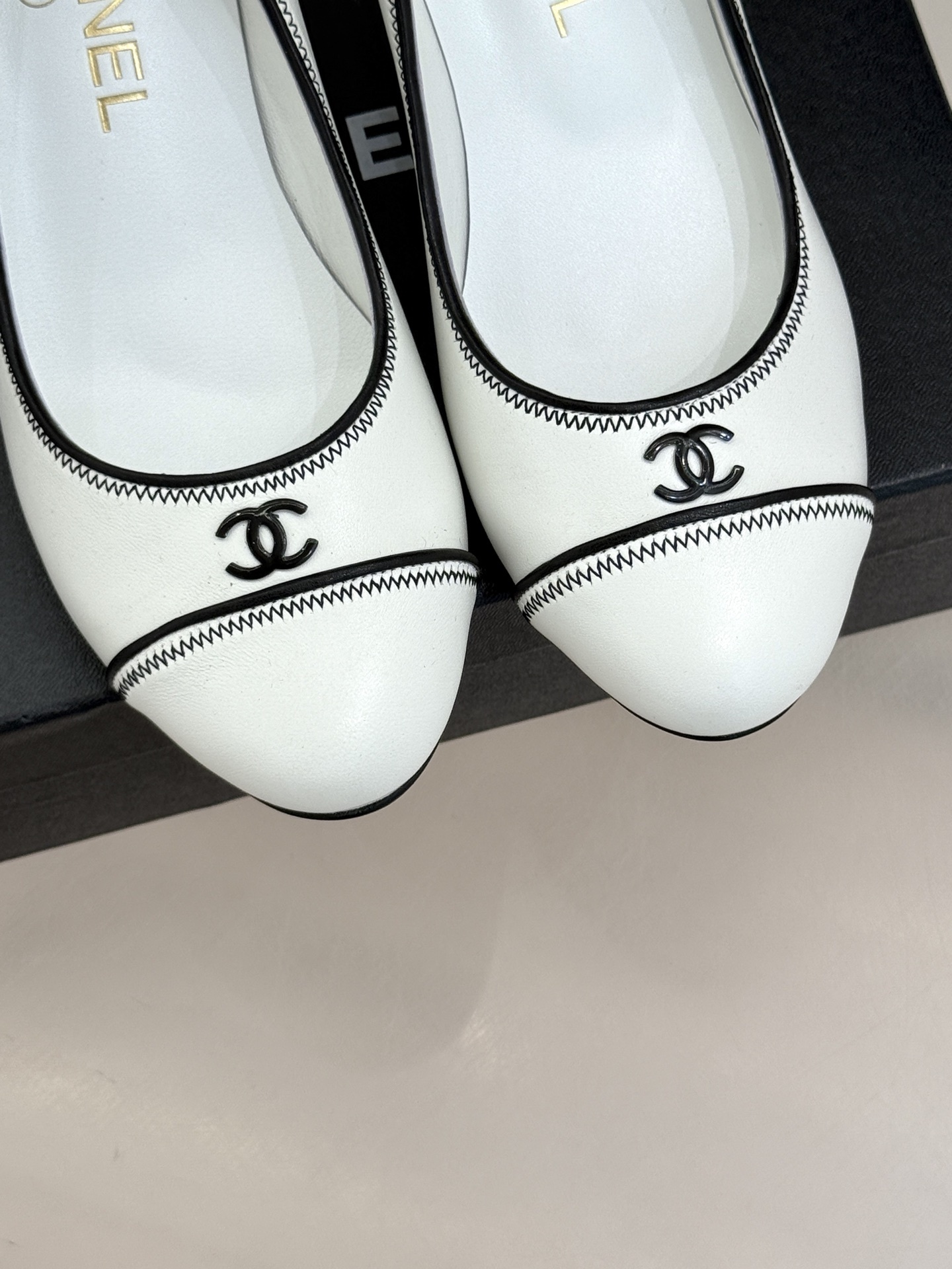 Elegant white Chanel kitten heels with black trim and CC logo on a black shoe box next to a quilted bag. - Hình 7
