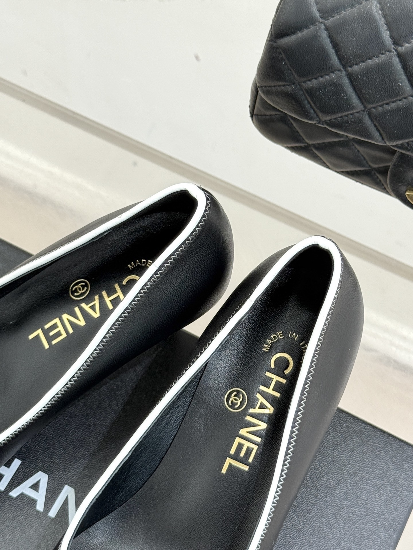 Elegant black Chanel leather pumps with white trim and CC logo resting on a black designer box - Hình 8