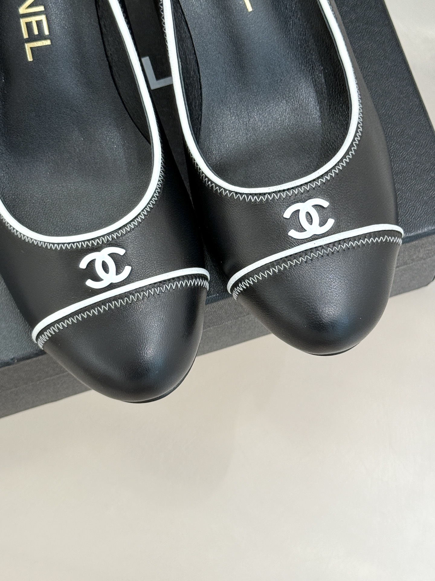 Elegant black Chanel leather pumps with white trim and CC logo resting on a black designer box - Hình 7