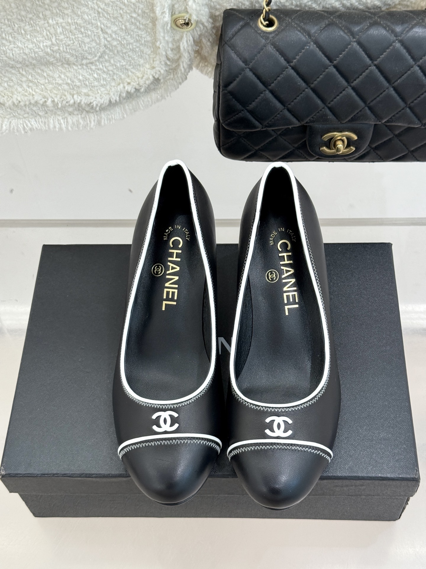 Elegant black Chanel leather pumps with white trim and CC logo resting on a black designer box - Hình 4