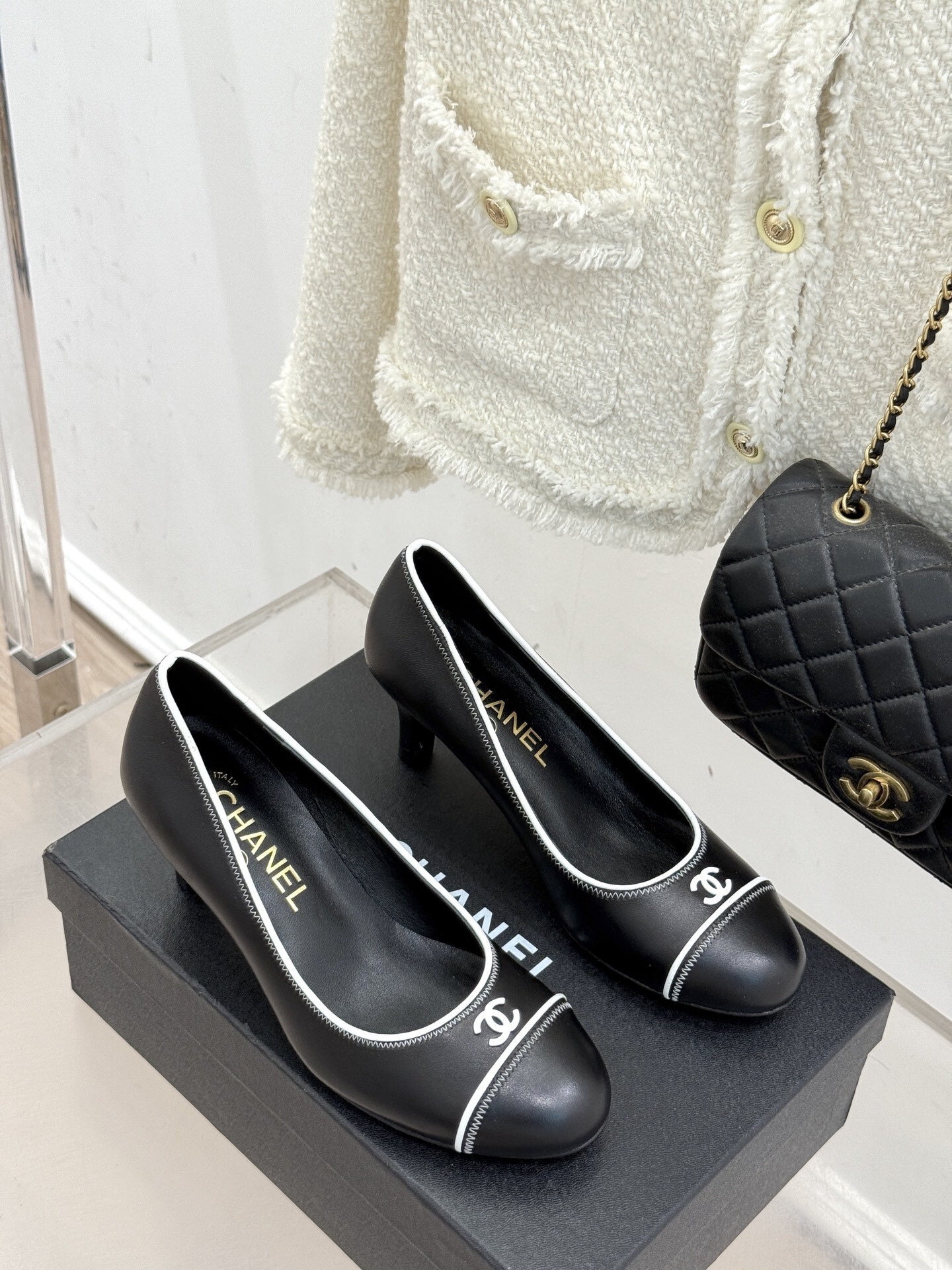 Elegant black Chanel leather pumps with white trim and CC logo resting on a black designer box - Hình 3