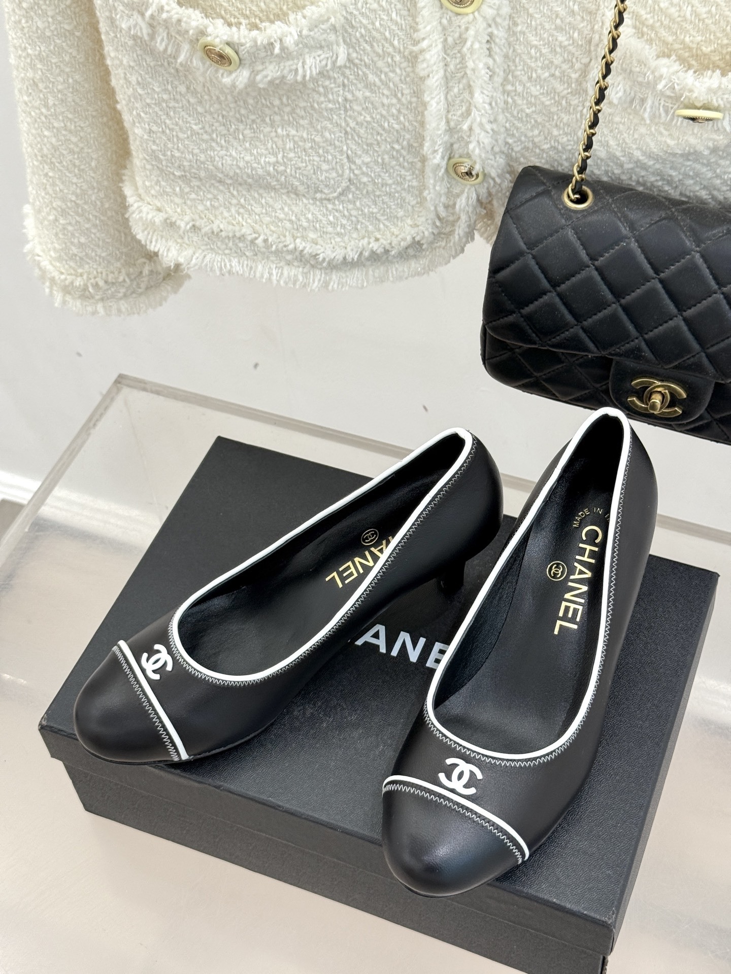 Elegant black Chanel leather pumps with white trim and CC logo resting on a black designer box - Hình 2