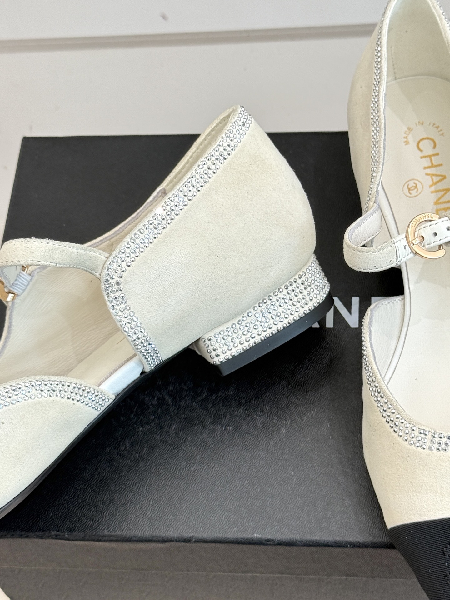 Luxury Chanel white suede Mary Jane flats with crystal trim and black cap toe displayed on a black designer box. - Hình 6