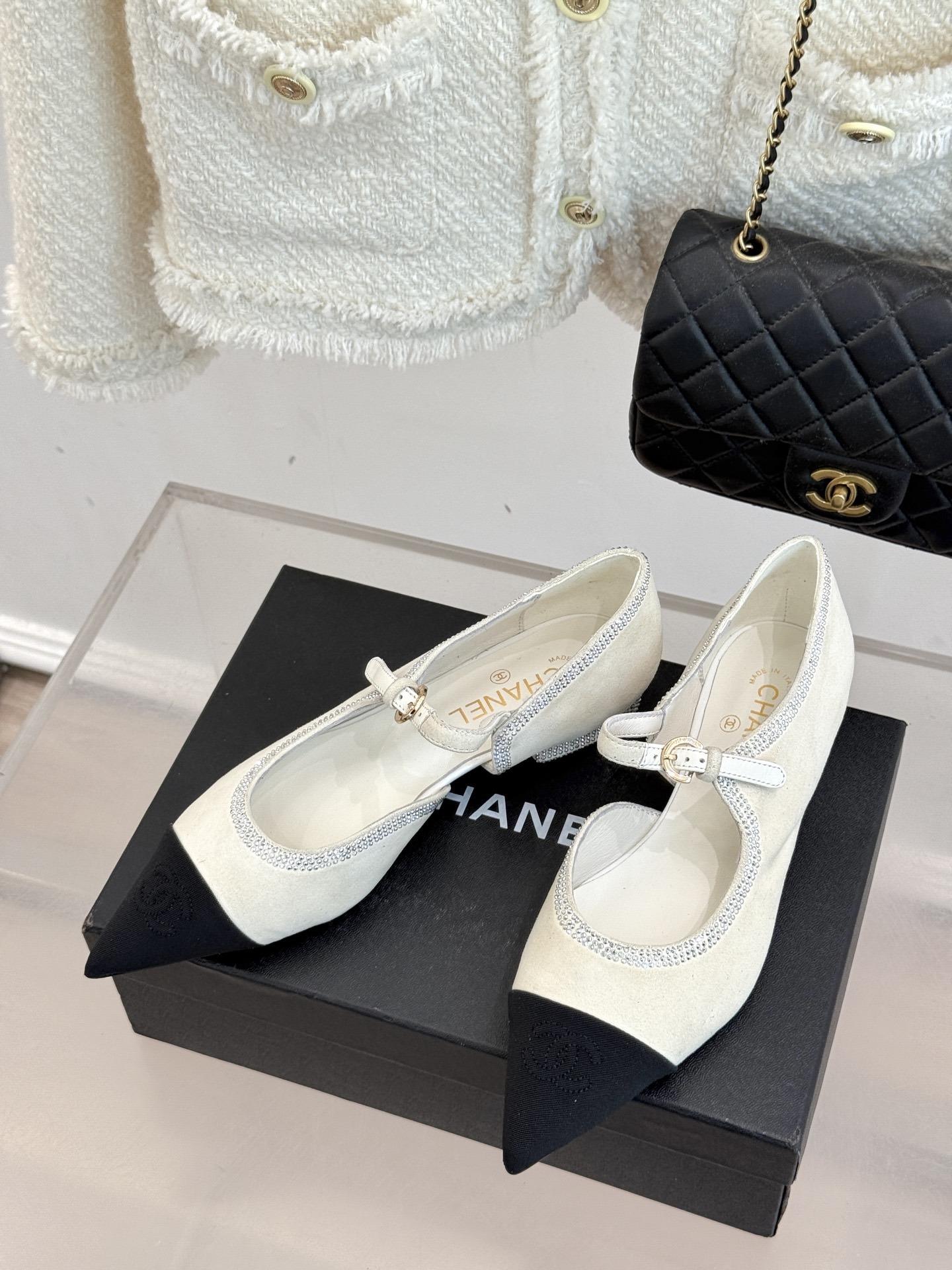 Luxury Chanel white suede Mary Jane flats with crystal trim and black cap toe displayed on a black designer box. - Hình 2
