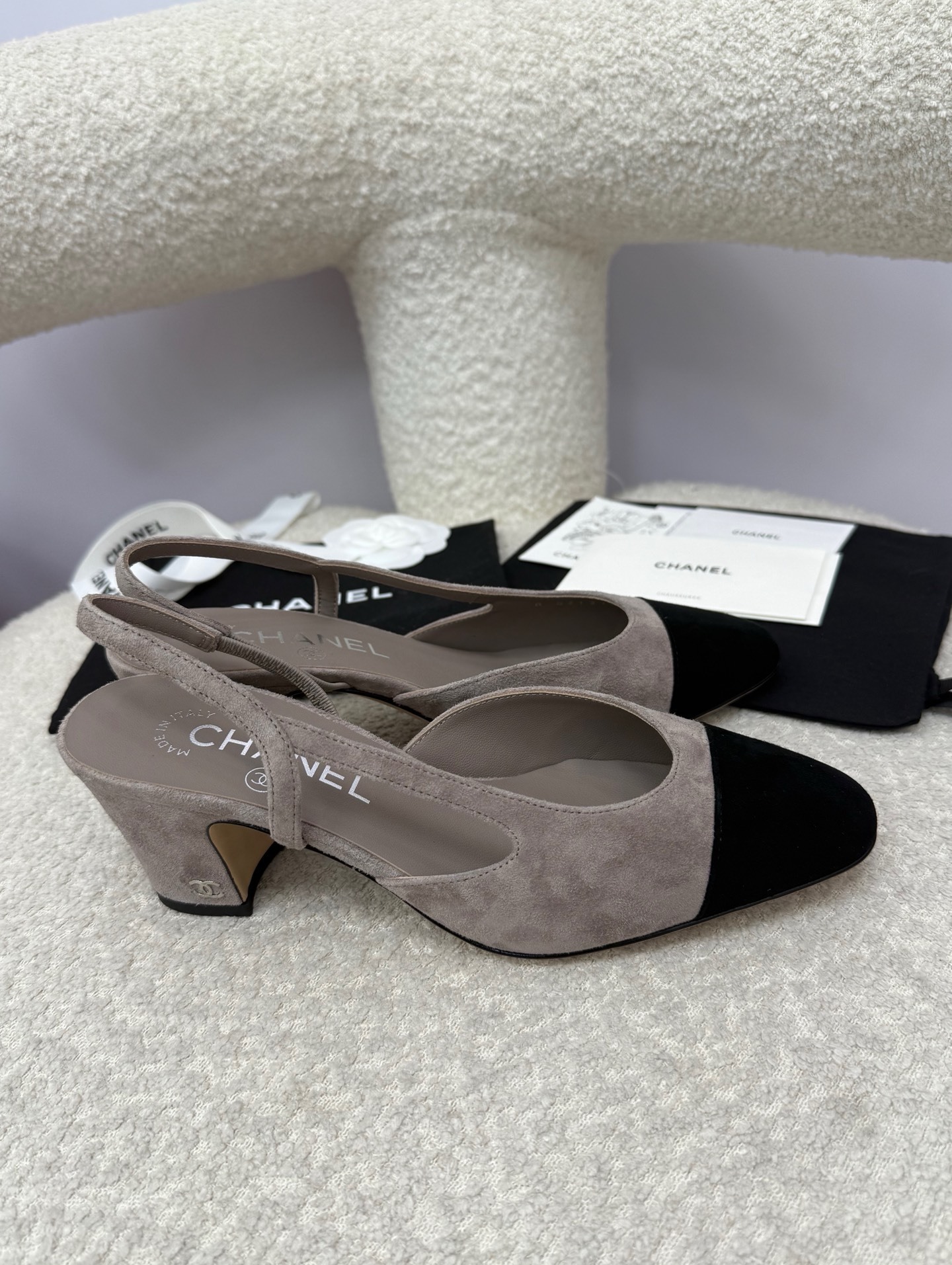 Chanel grey suede slingback pumps with black cap toe and block heel displayed on a white textured chair - Hình 8