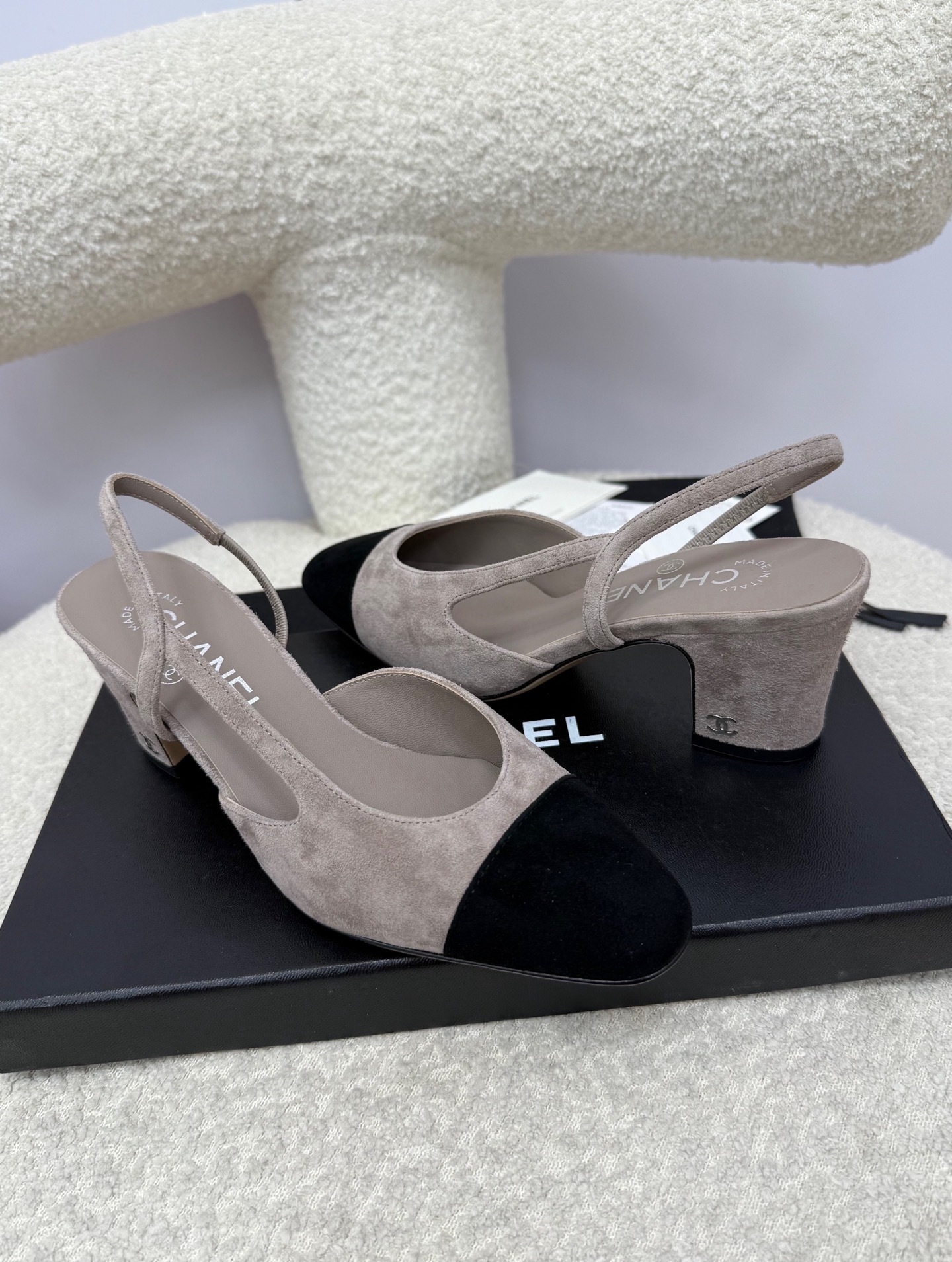 Chanel grey suede slingback pumps with black cap toe and block heel displayed on a white textured chair - Hình 7